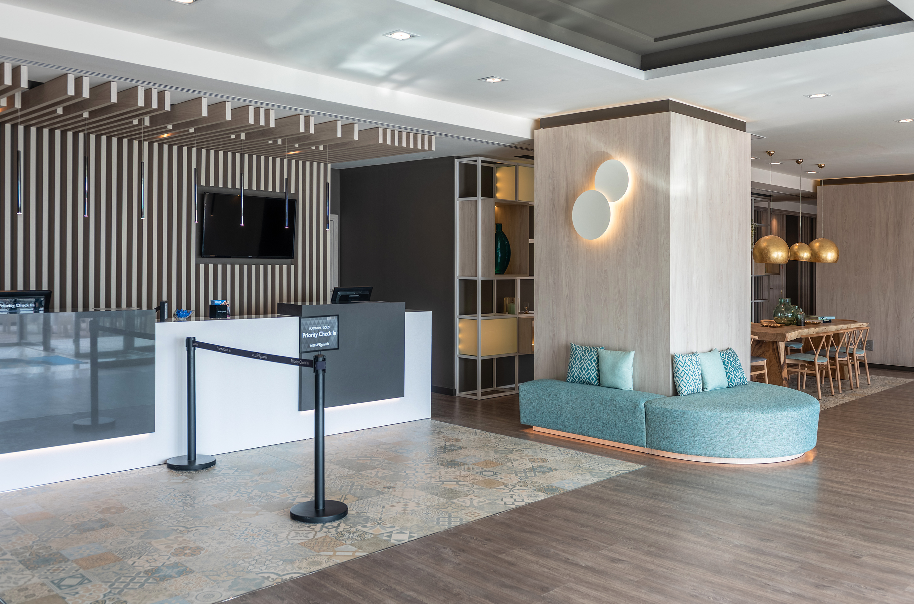 Modern hotel lobby with reception, priority check-in, and teal lounge seating.