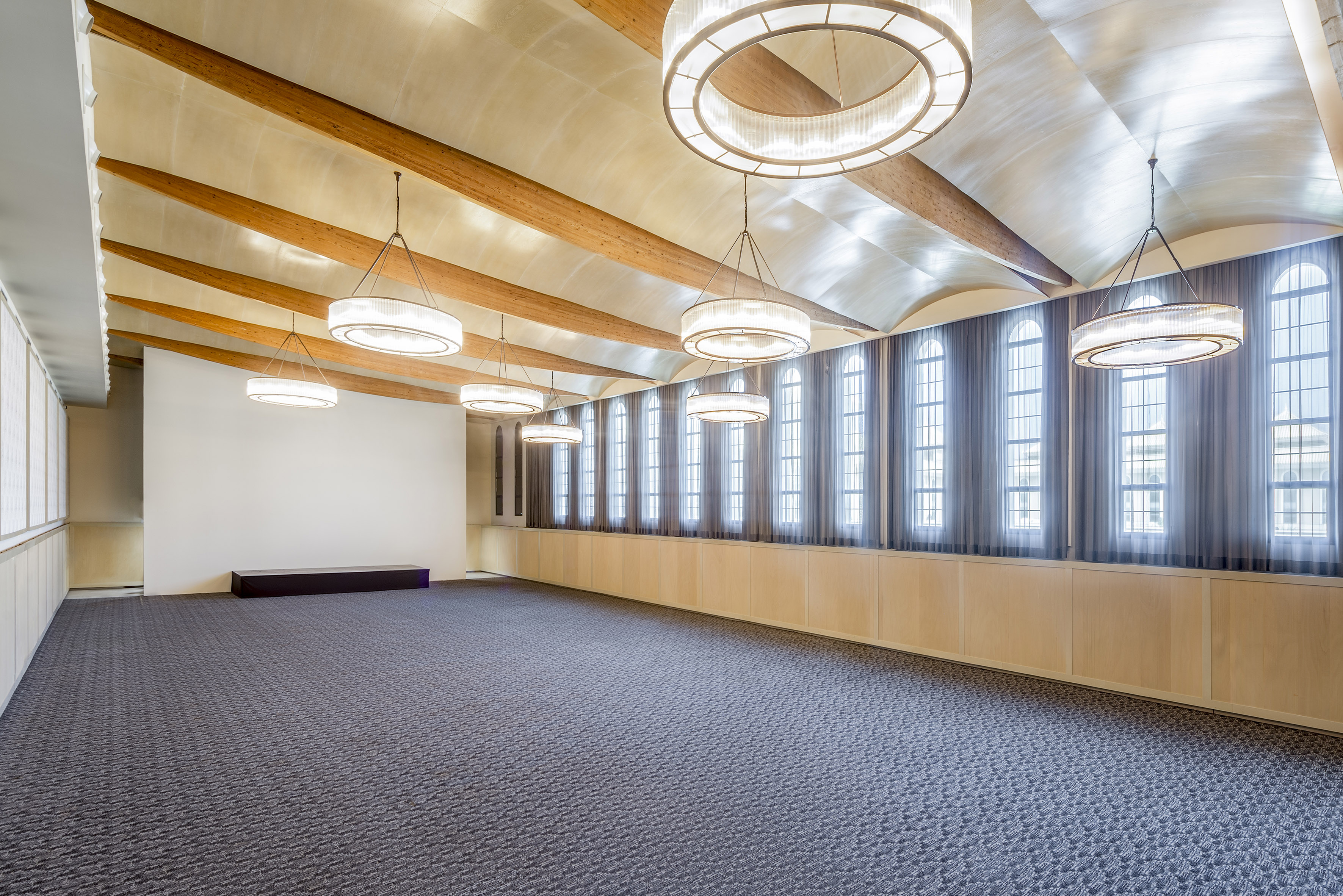 Modern event hall with arched windows, wood beams, and contemporary chandeliers.