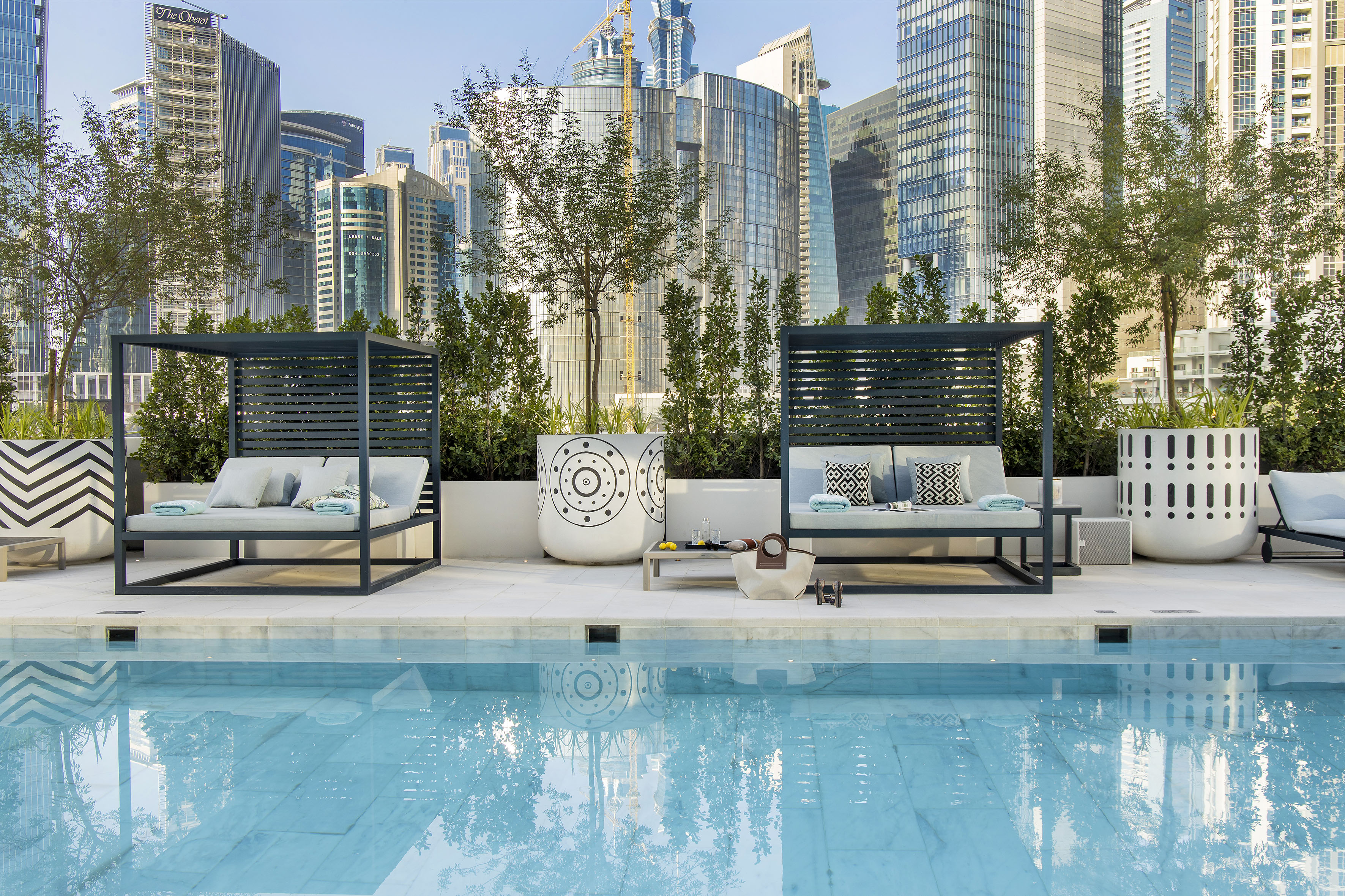 Rooftop pool with modern cabanas, city skyline, and lush greenery.