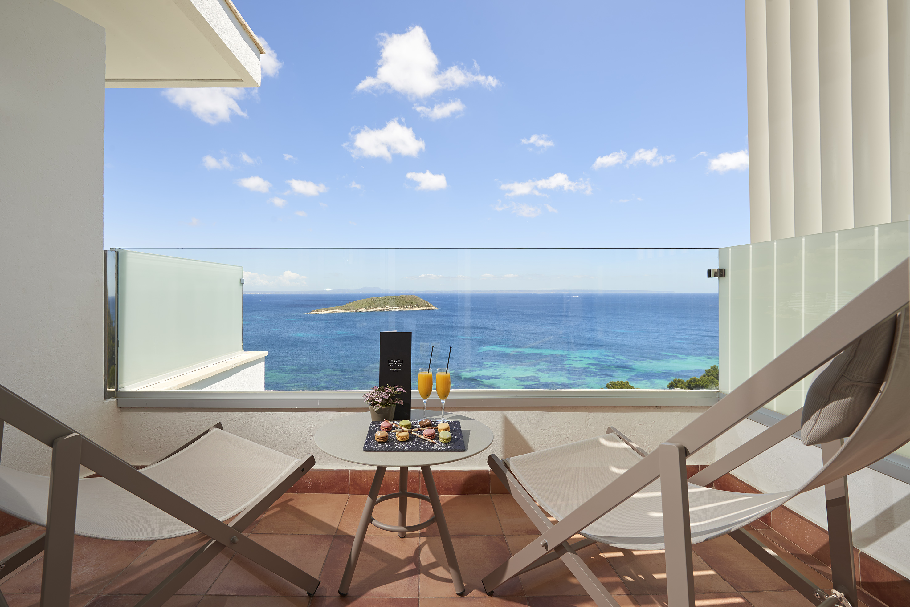 Hotel balcony ocean view with chairs, macarons, and fresh juice.