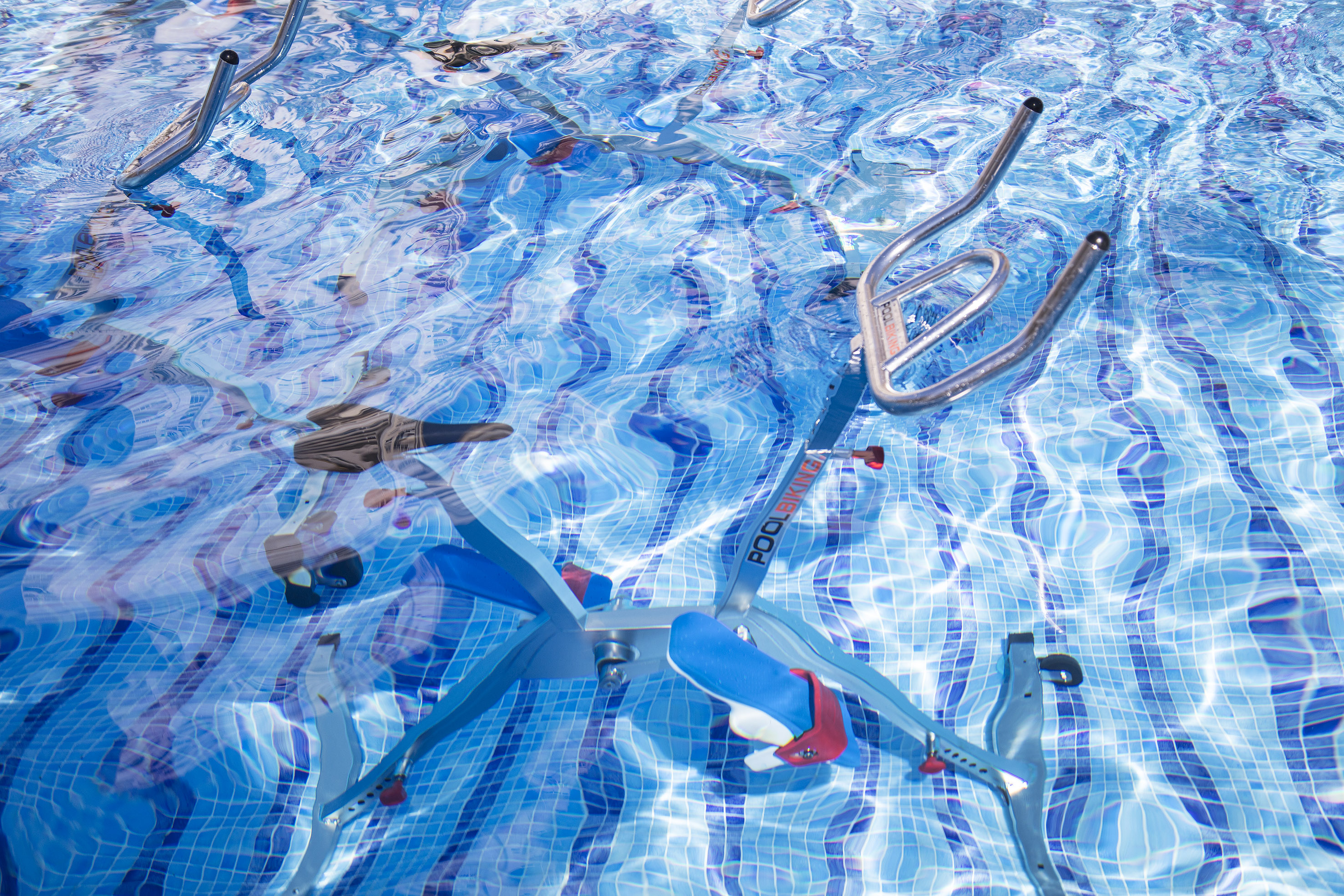 Blue aqua bike submerged in a swimming pool with rippling blue tiles.