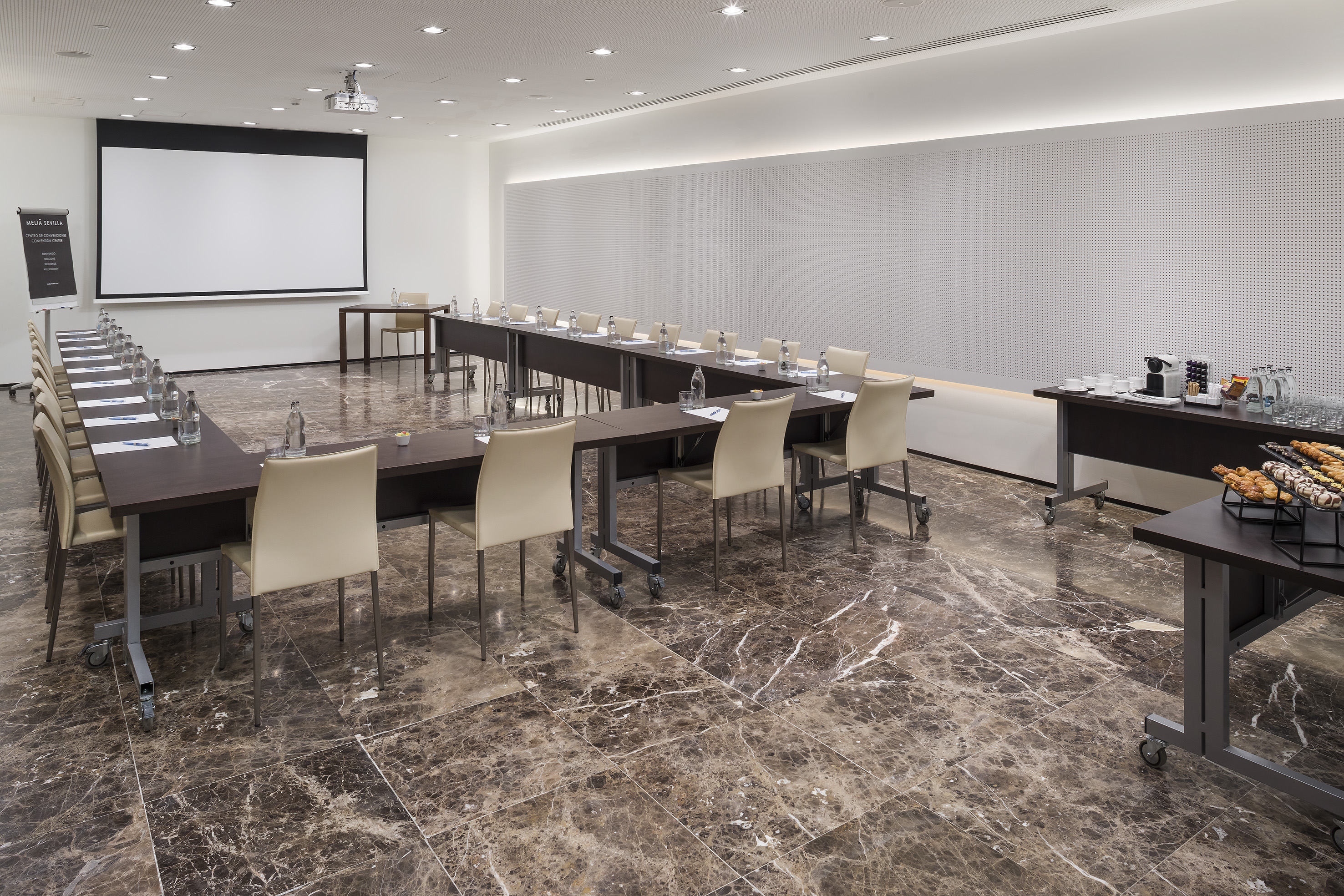 U-shaped conference room with projection screen, dark tables, and refreshment bar.