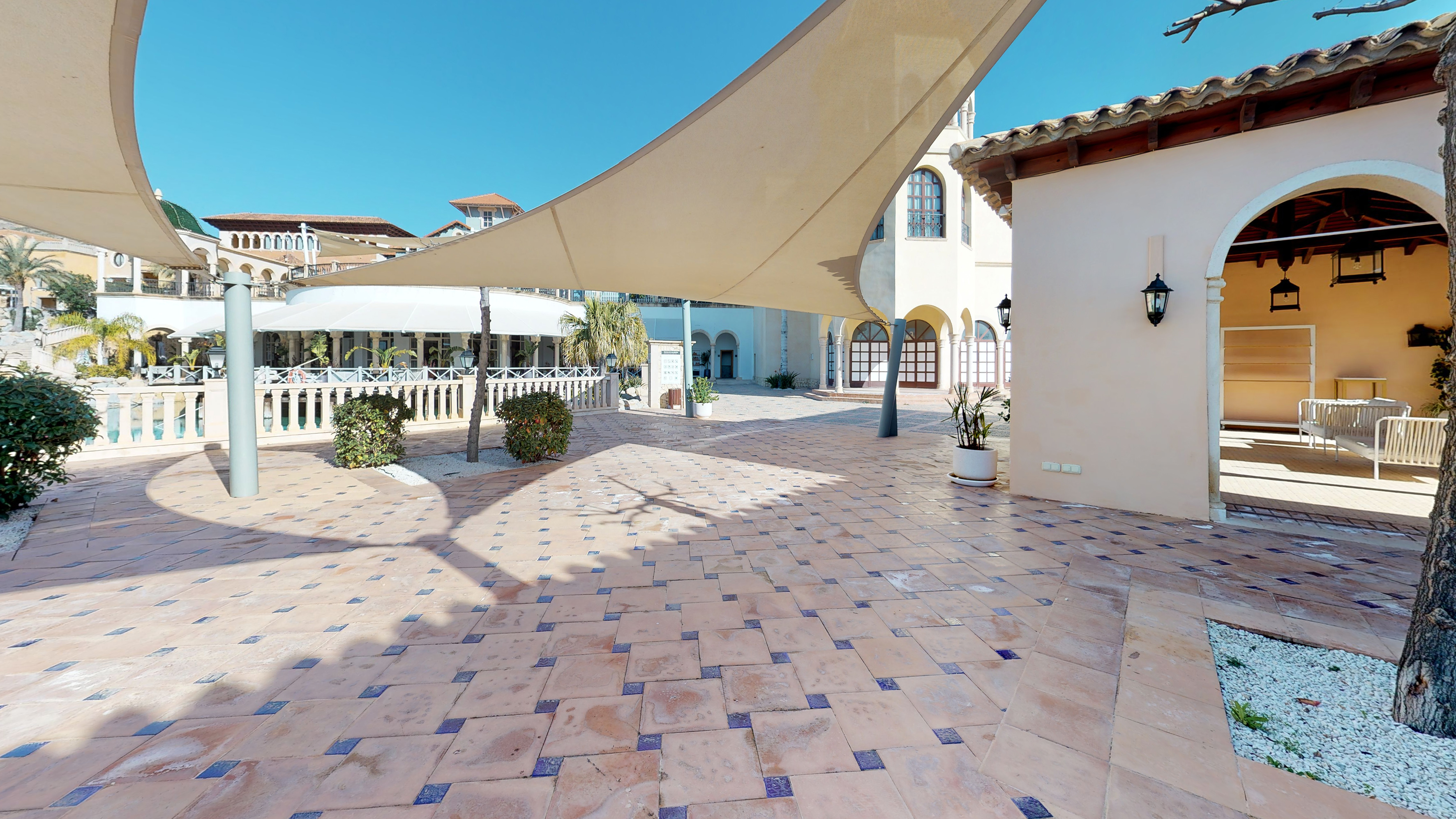 Mediterranean tiled patio with shade sails and resort architecture.
