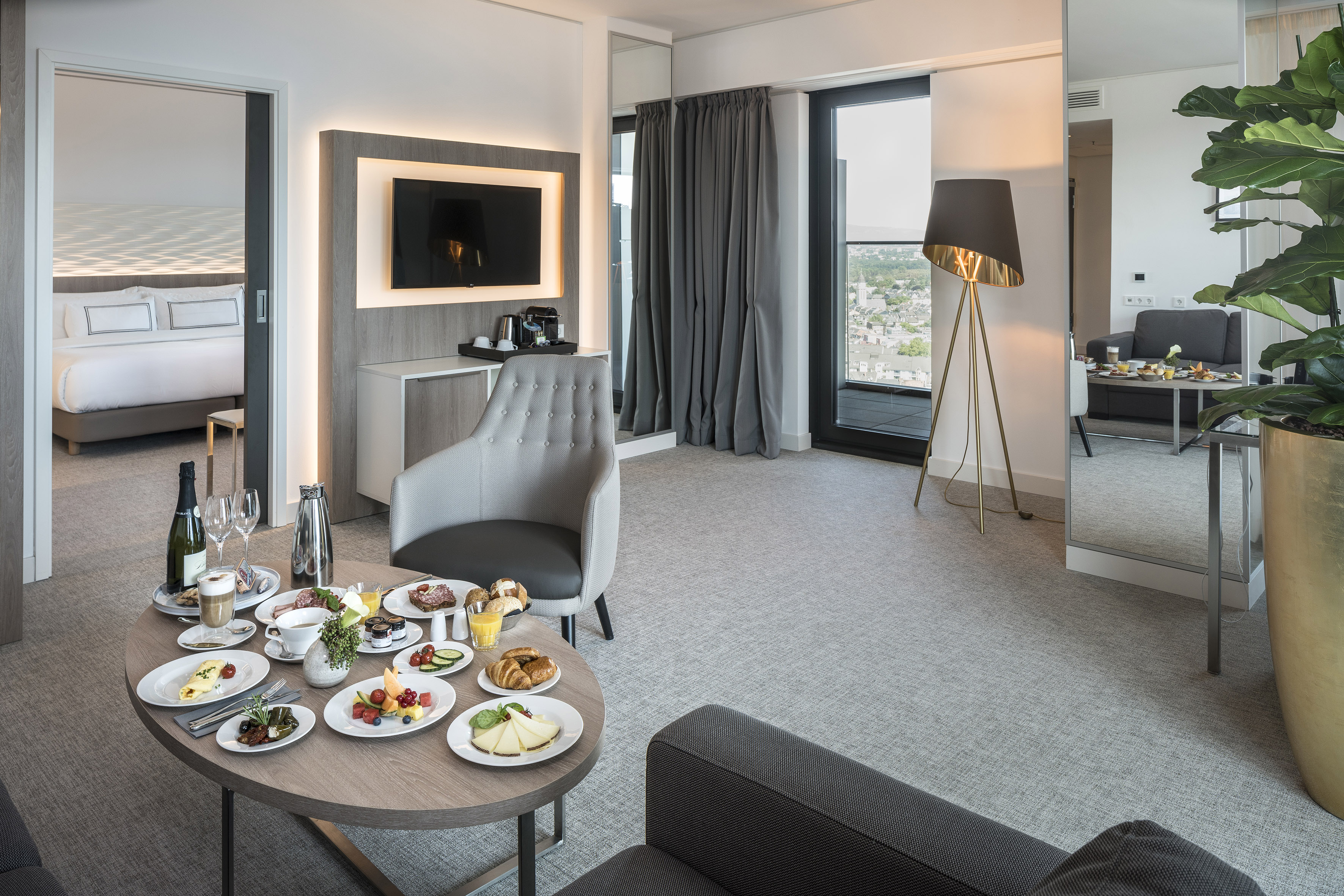 Hotel suite with in-room breakfast, modern decor, city view, and bedroom.