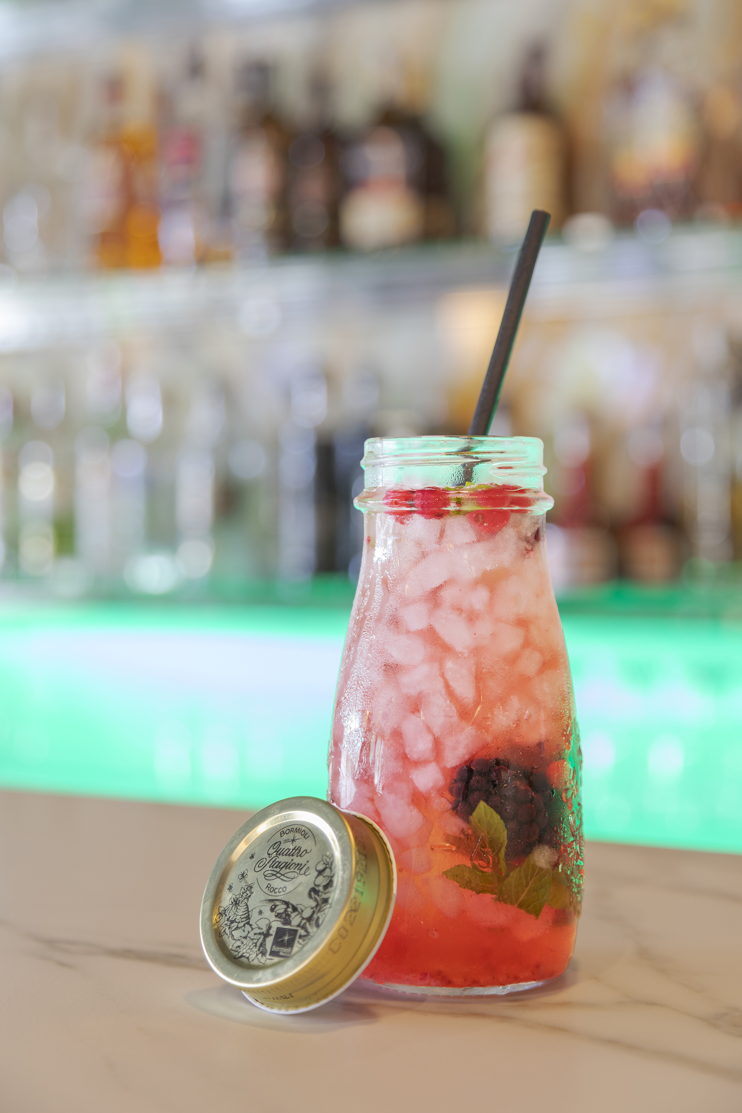 Iced berry cocktail with mint and straw in a jar at a bar.