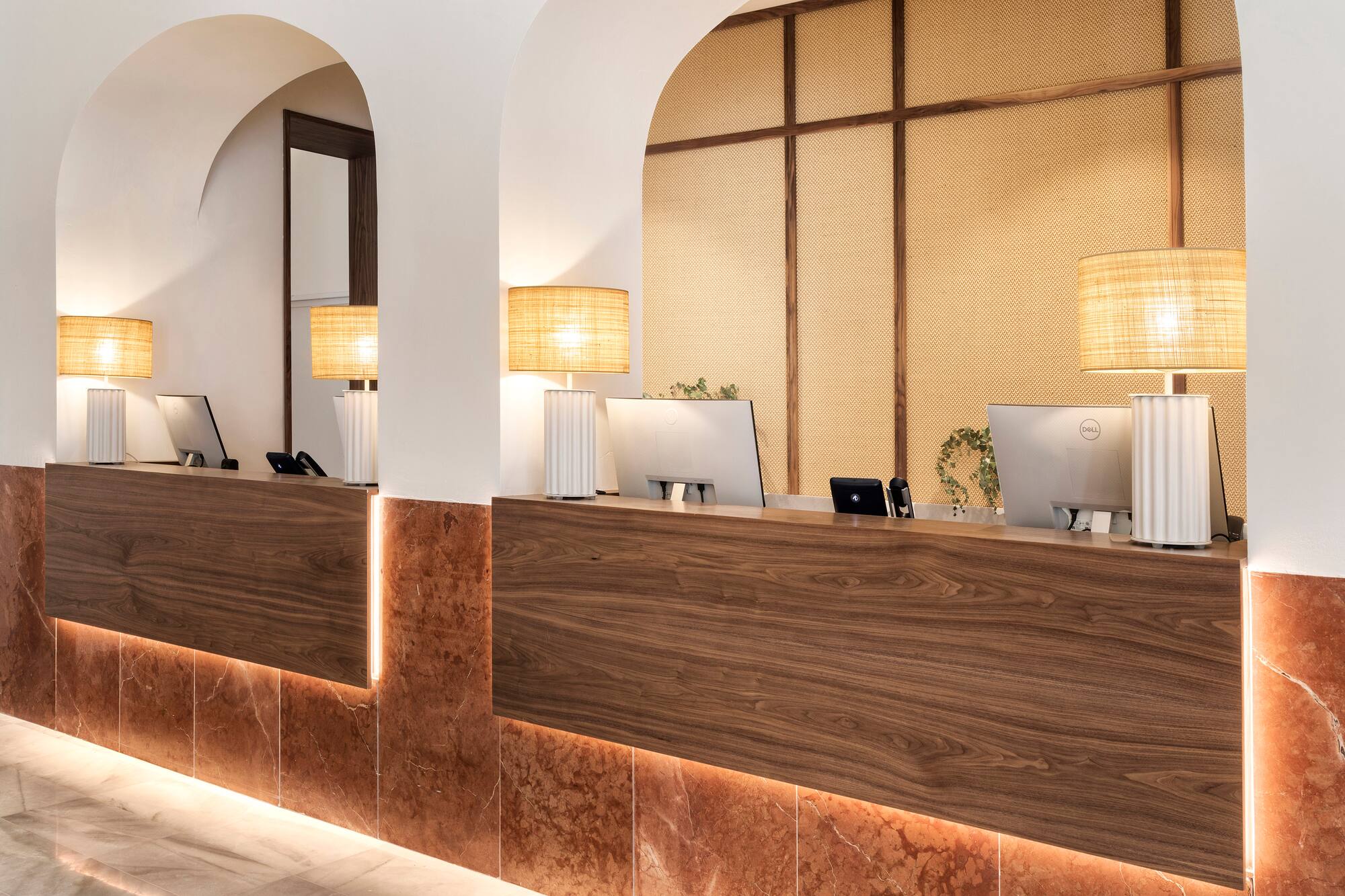 Modern hotel reception desk with wood, illuminated marble, arches, and computers.
