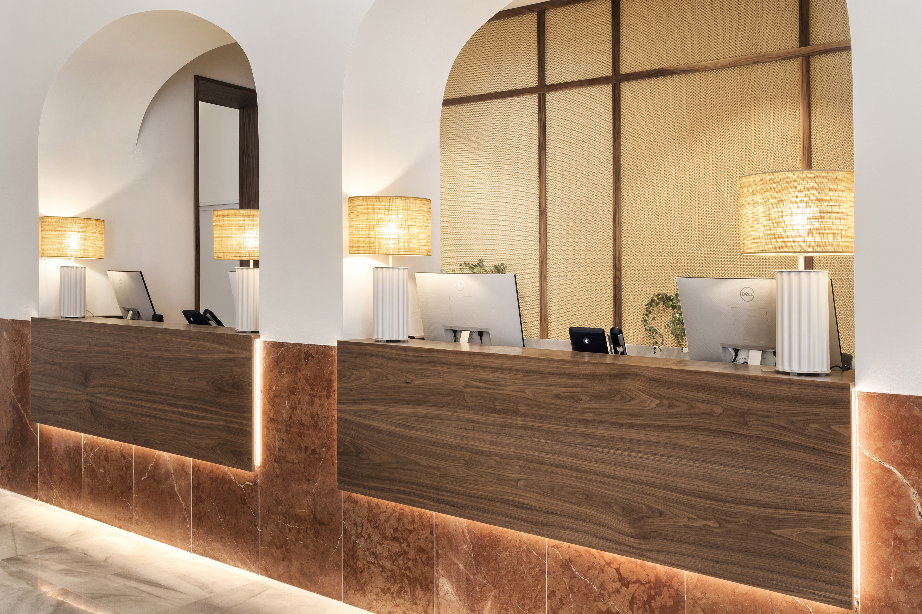 Modern hotel reception desk with wood, illuminated marble, arches, and computers.