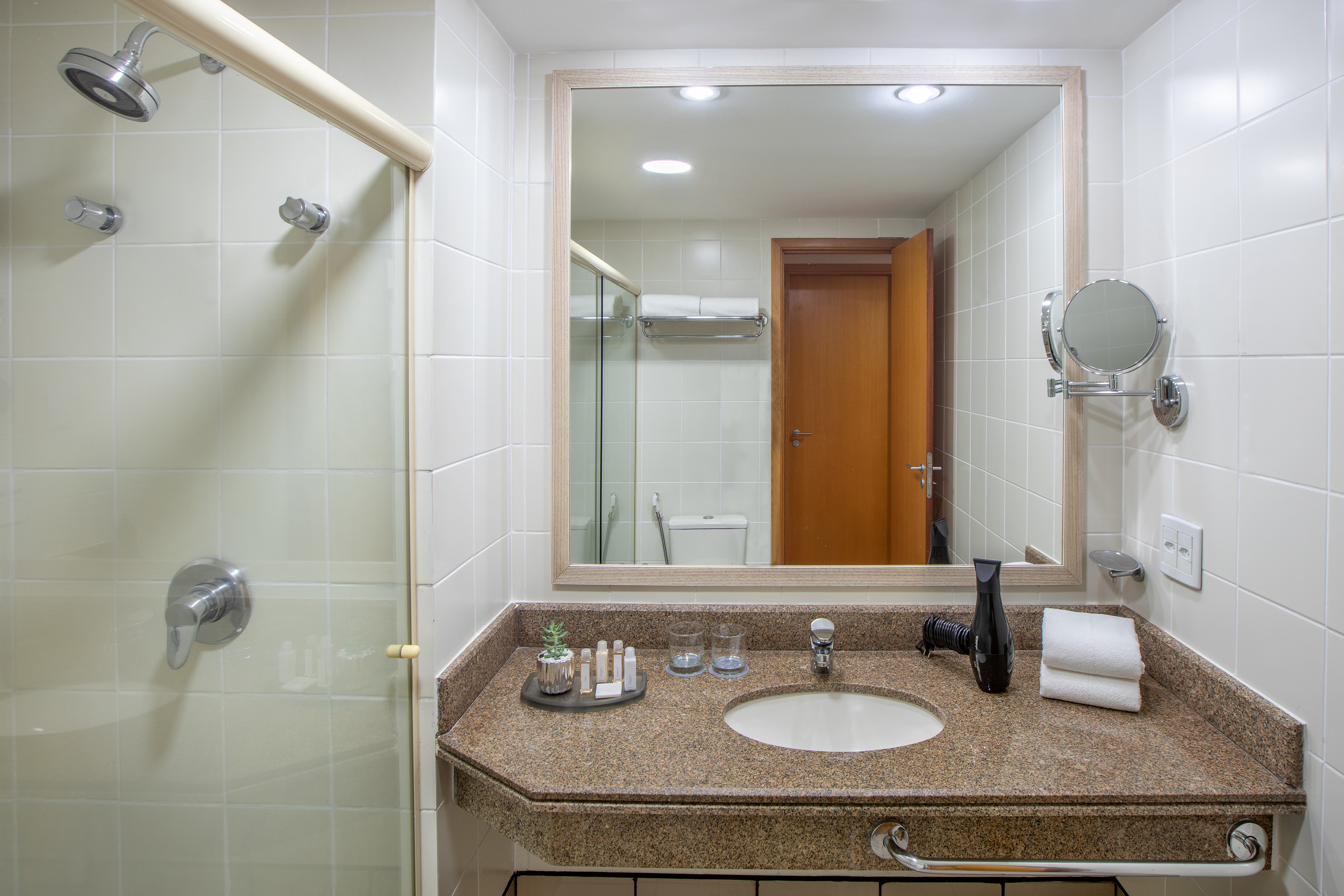 Hotel bathroom vanity with granite counter, sink, mirror, and shower.