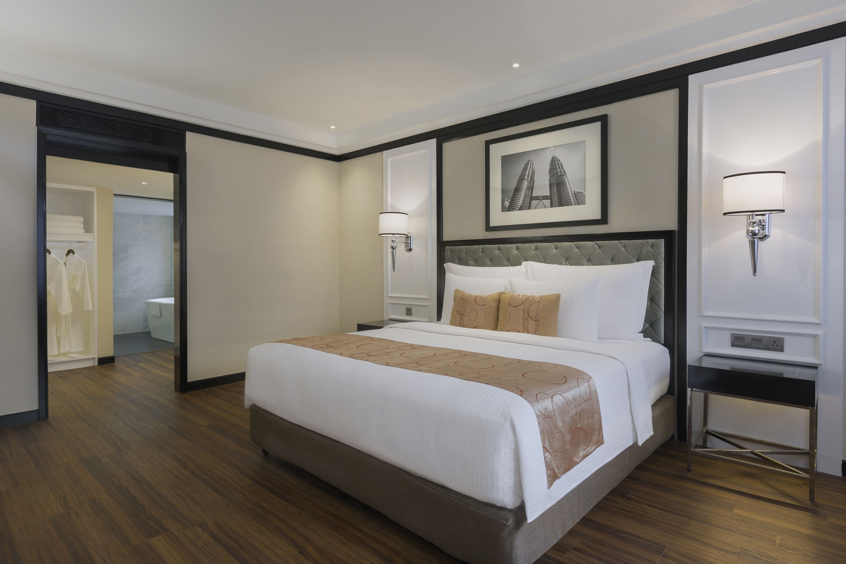 Hotel room with king bed, Petronas Towers art, wood floor, open closet.
