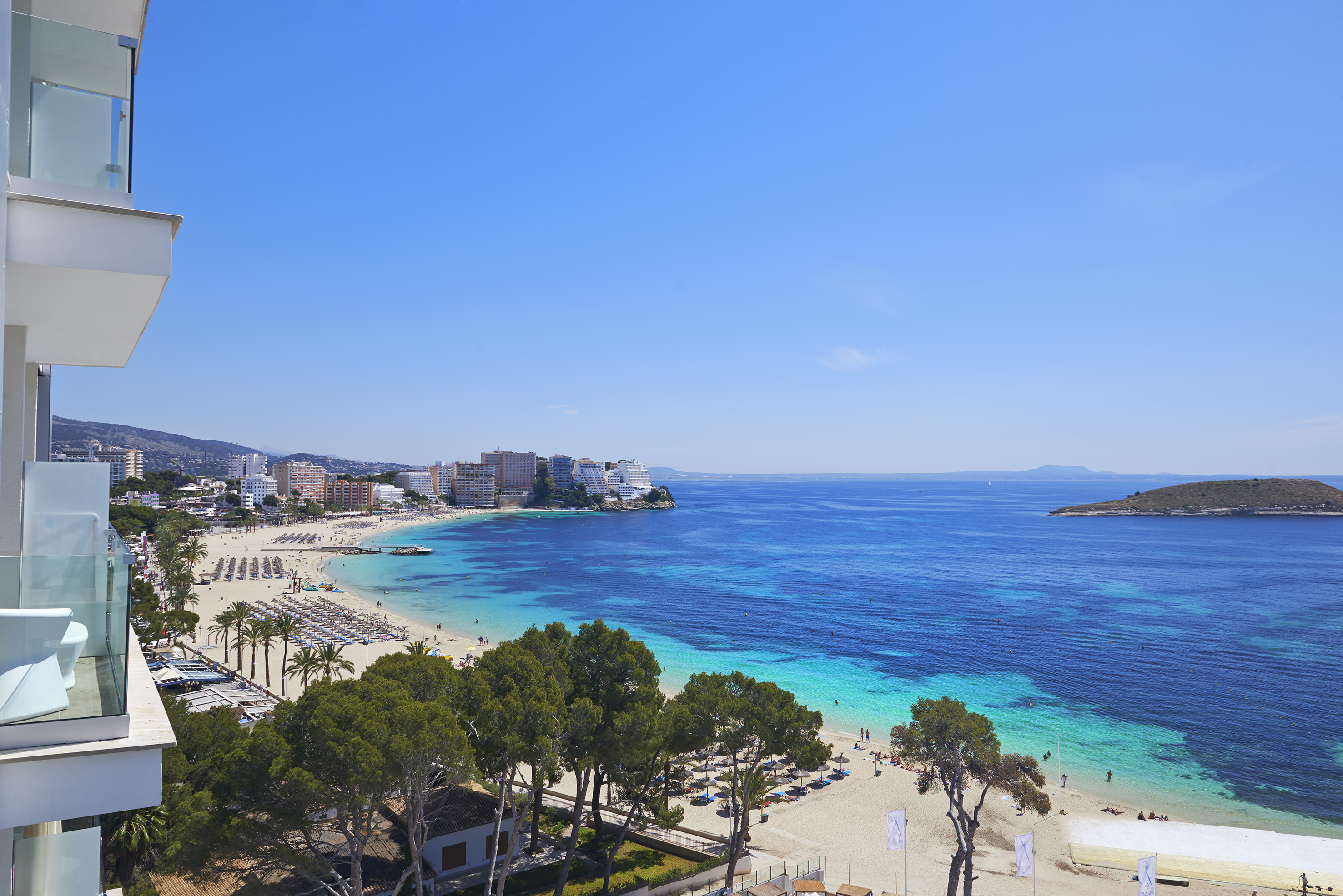 Panoramic beach resort bay with turquoise ocean, sandy shore, palm trees, hotels.