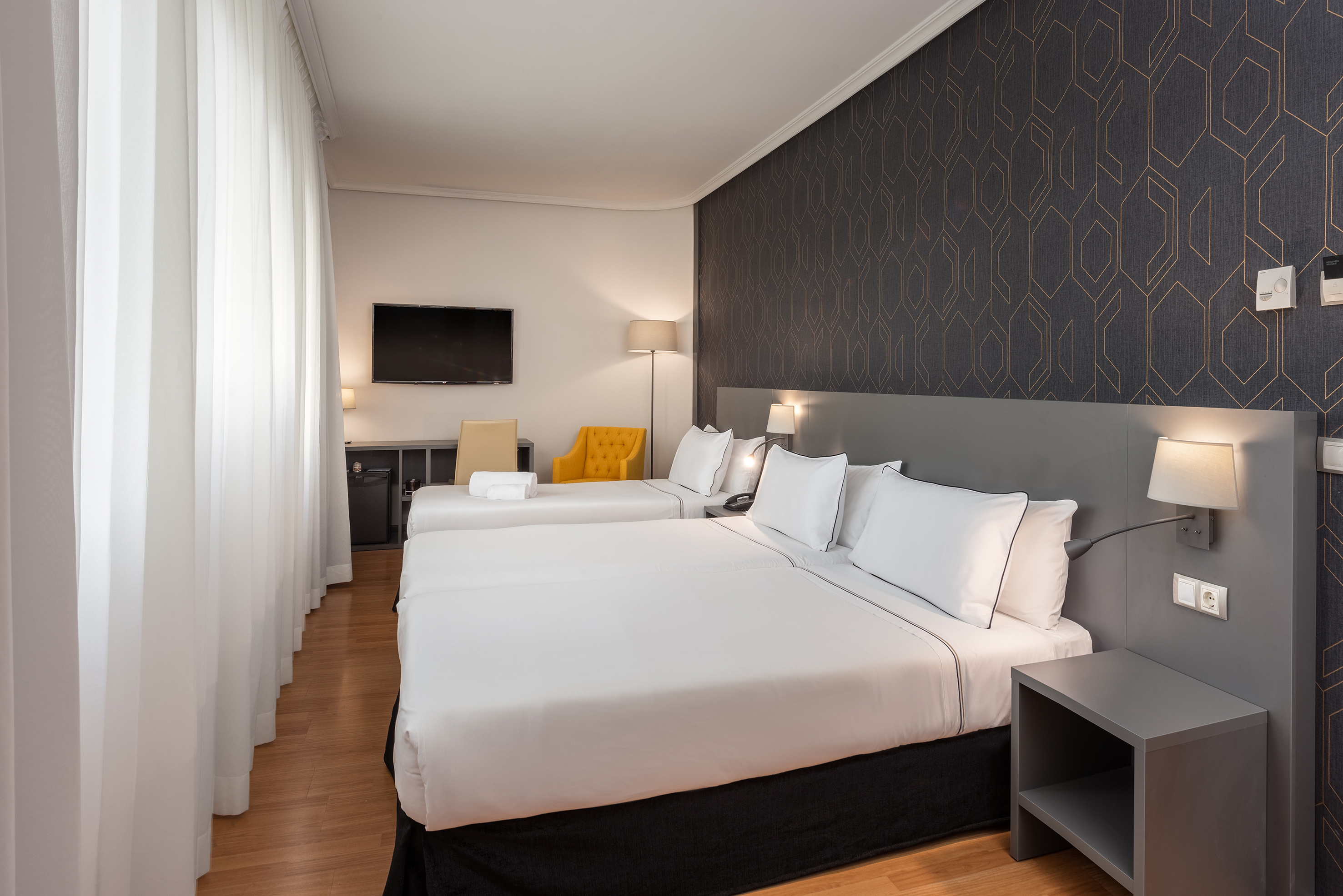Clean, modern hotel room with two beds, TV, and yellow armchair.