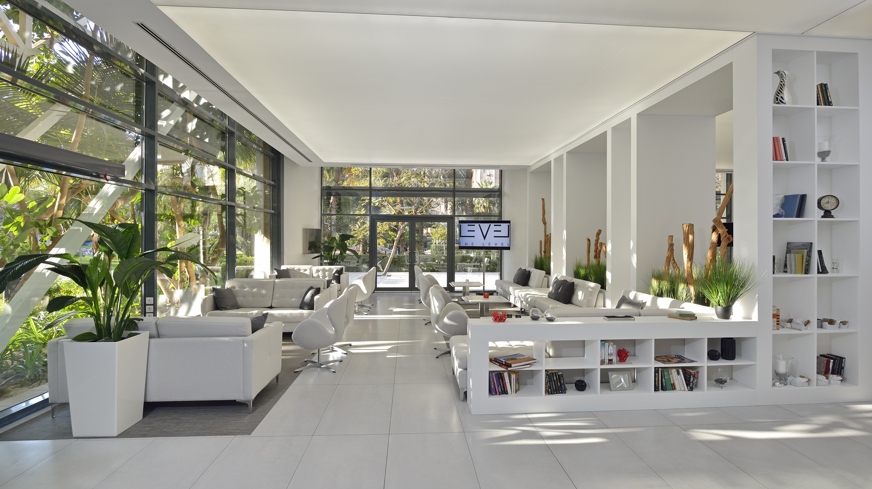 Bright modern hotel lounge with white sofas, large windows, and green garden.