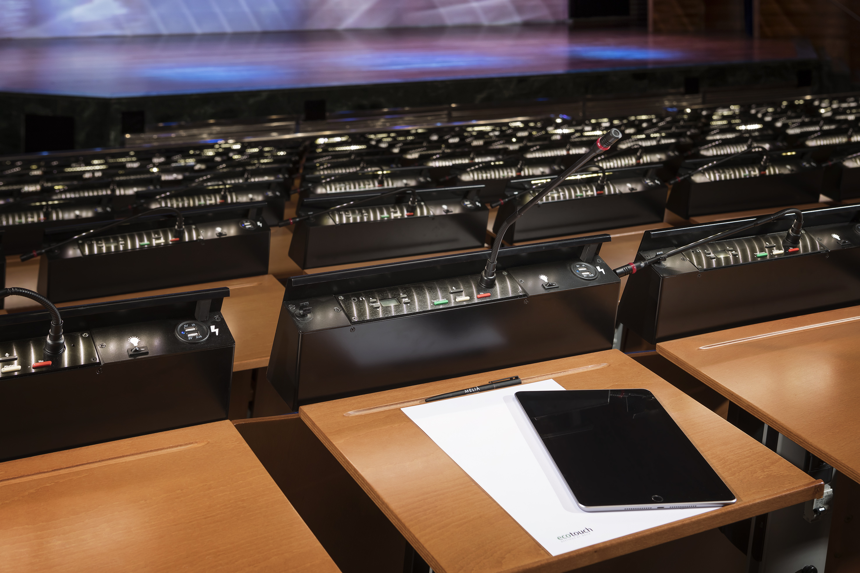 Empty conference room desks with microphones, control panels, tablet, and pen.