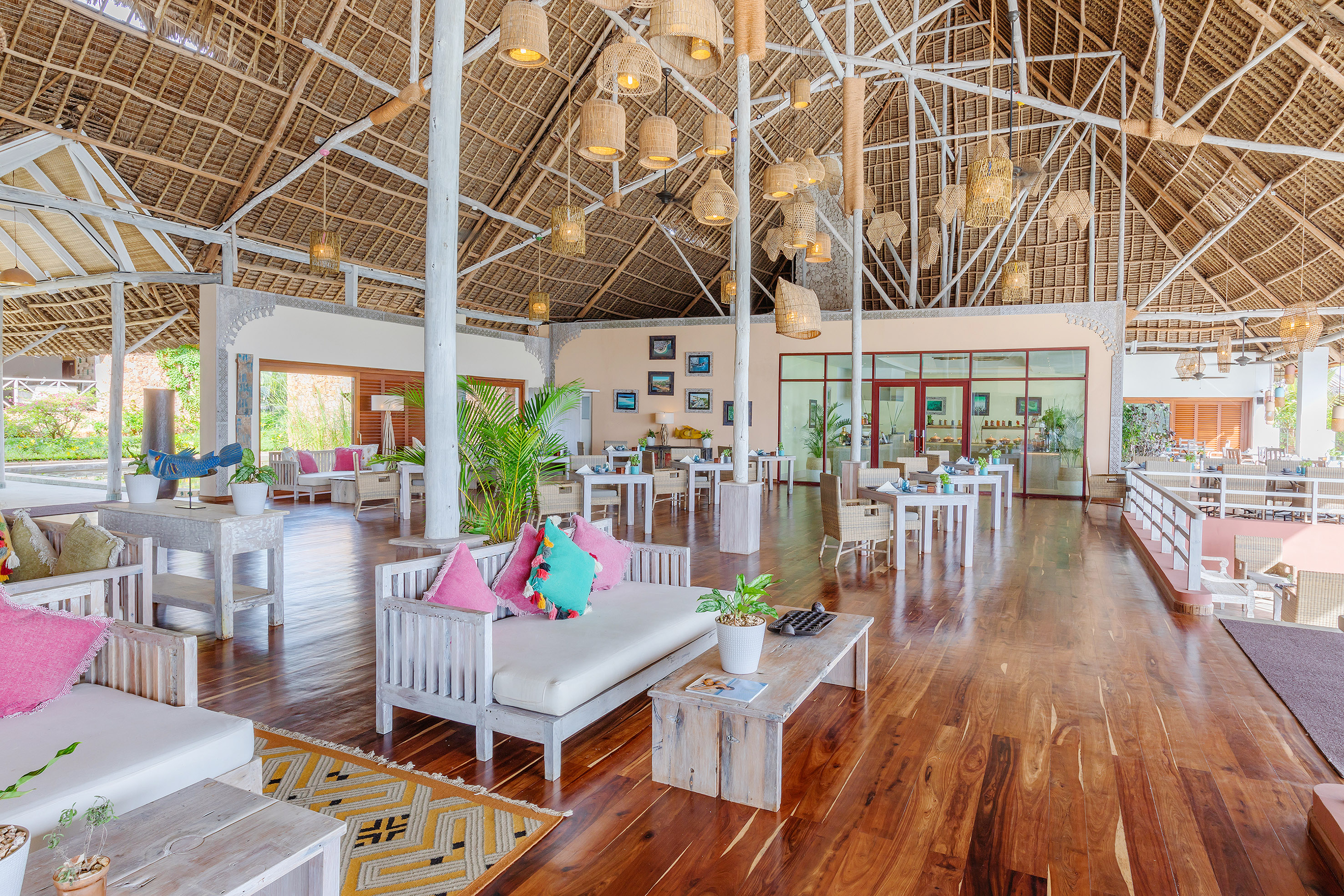 Tropical resort restaurant with thatched roof, wooden floors, and woven pendant lights.