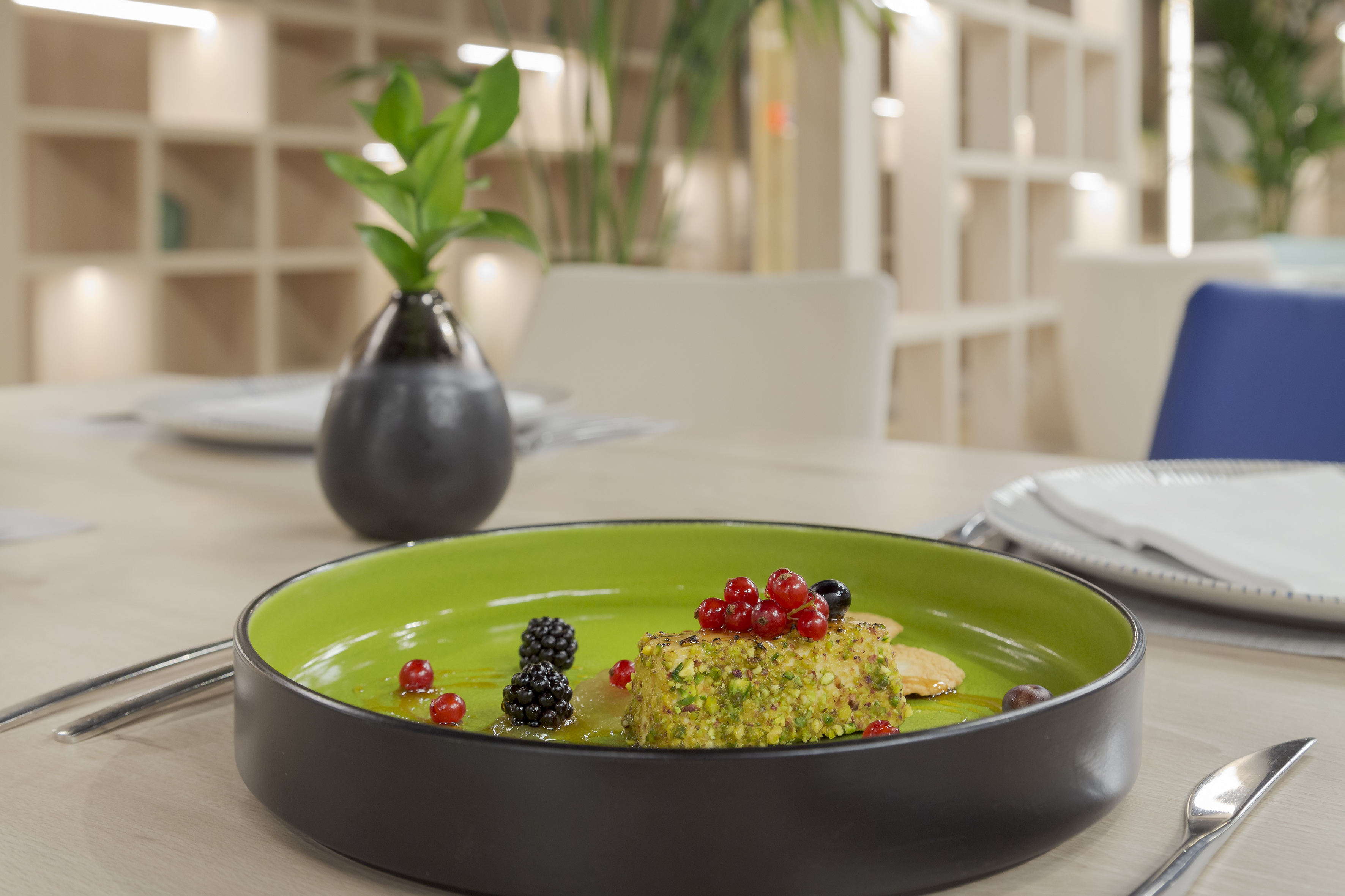 Pistachio dessert with berries on green plate in modern restaurant setting.