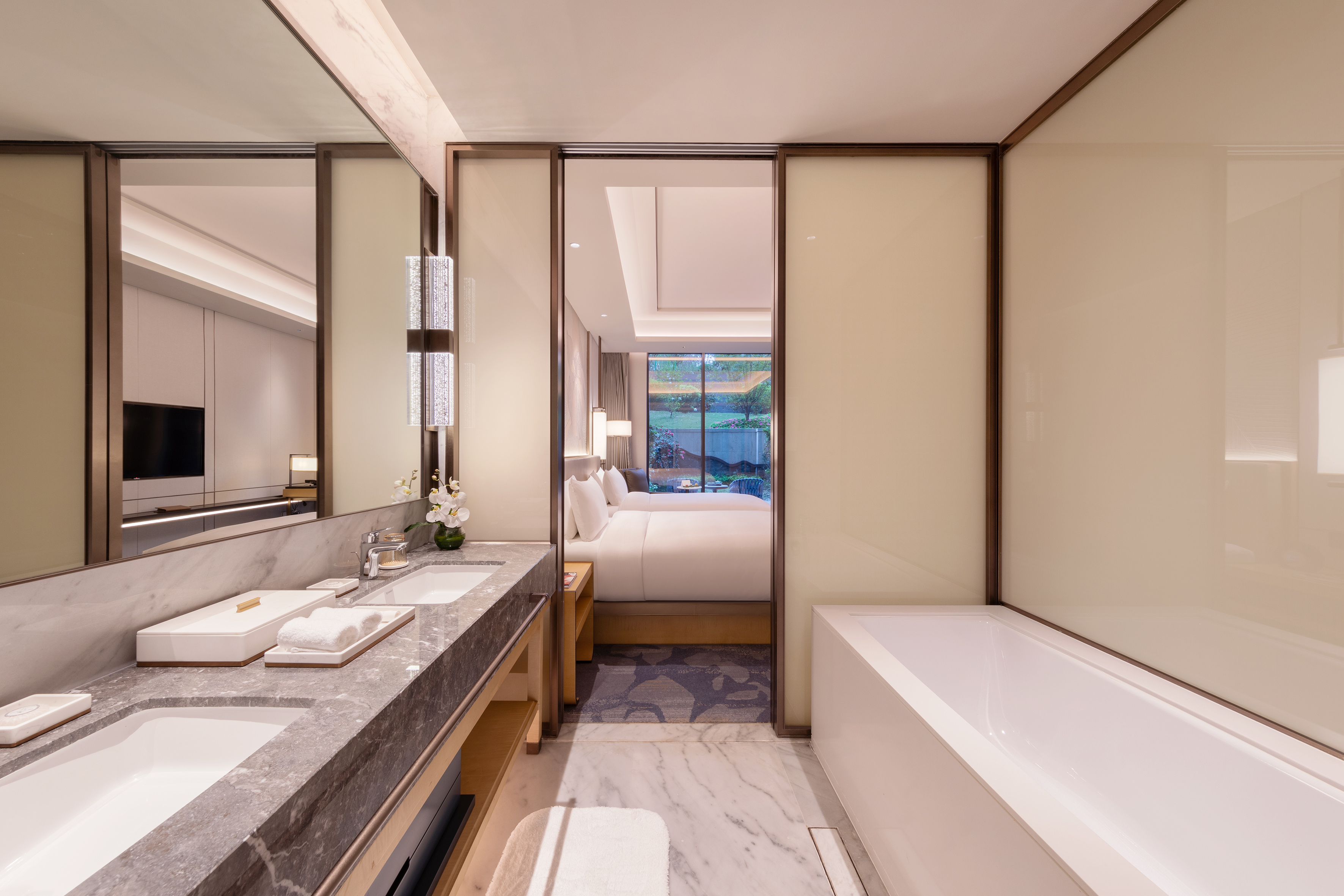 Modern luxury hotel bathroom, double marble vanity, bathtub, bedroom view.