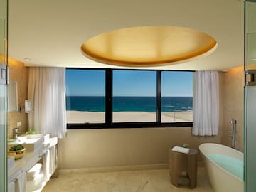 a bathroom with a tub and a sink and a window overlooking the ocean
