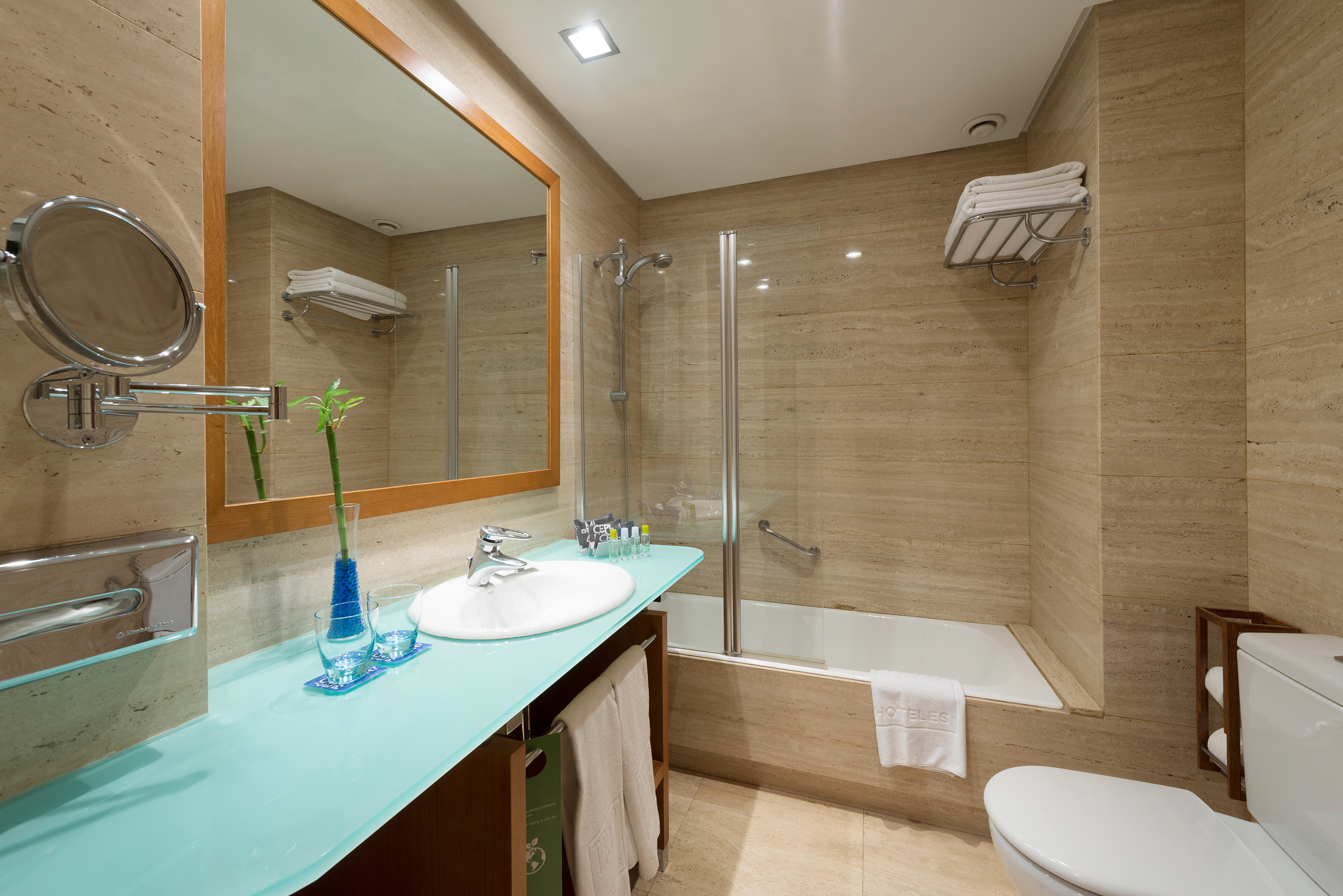 Modern hotel bathroom with blue vanity, beige tiles, sink, bathtub, and shower.