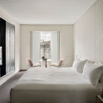 a bed with white sheets and a table and chairs in a room