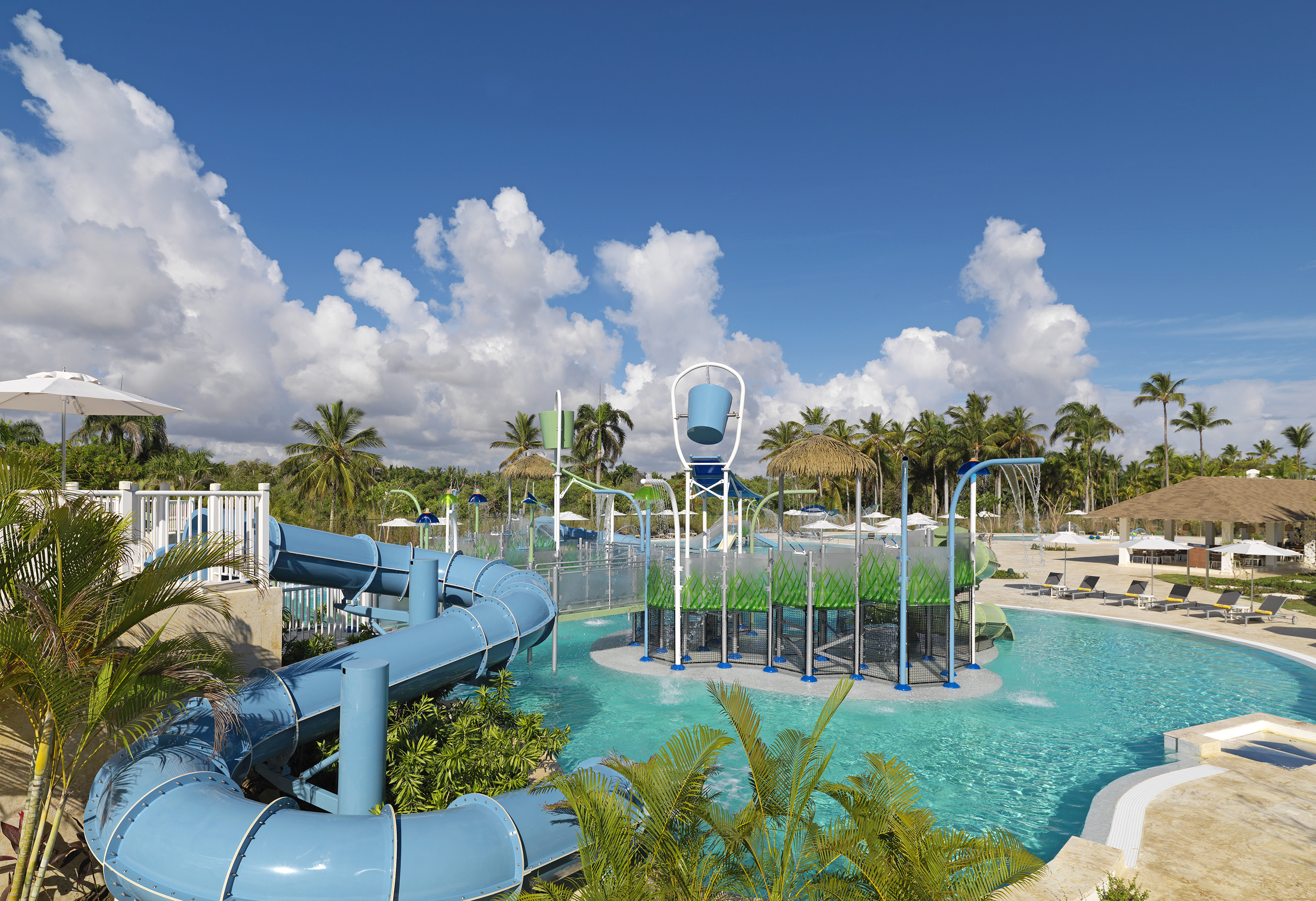 Tropical resort water park with blue slides, splash pad, and palm trees.