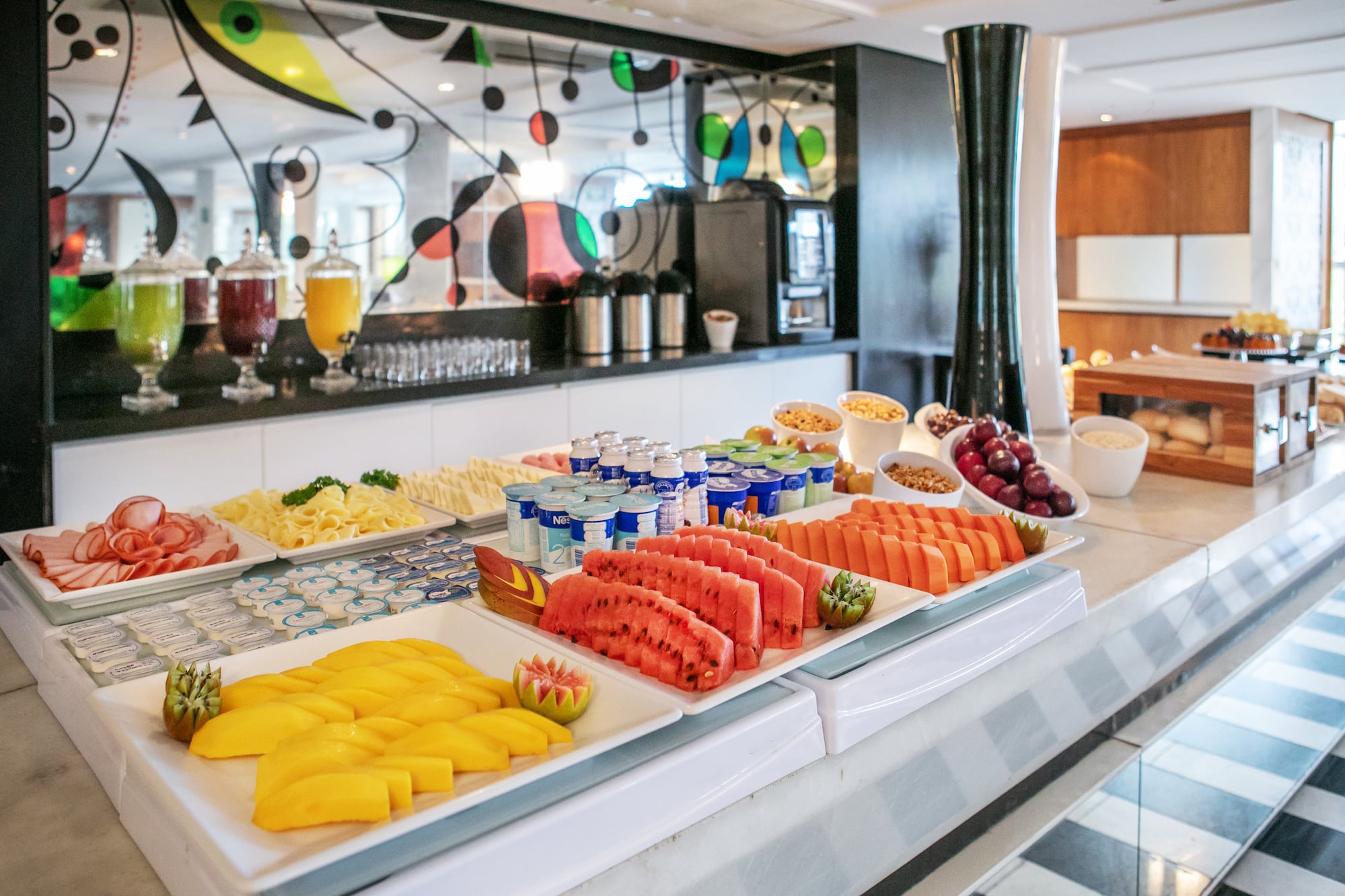 Vibrant hotel breakfast buffet with fresh fruit, cold cuts, yogurt, and juices.