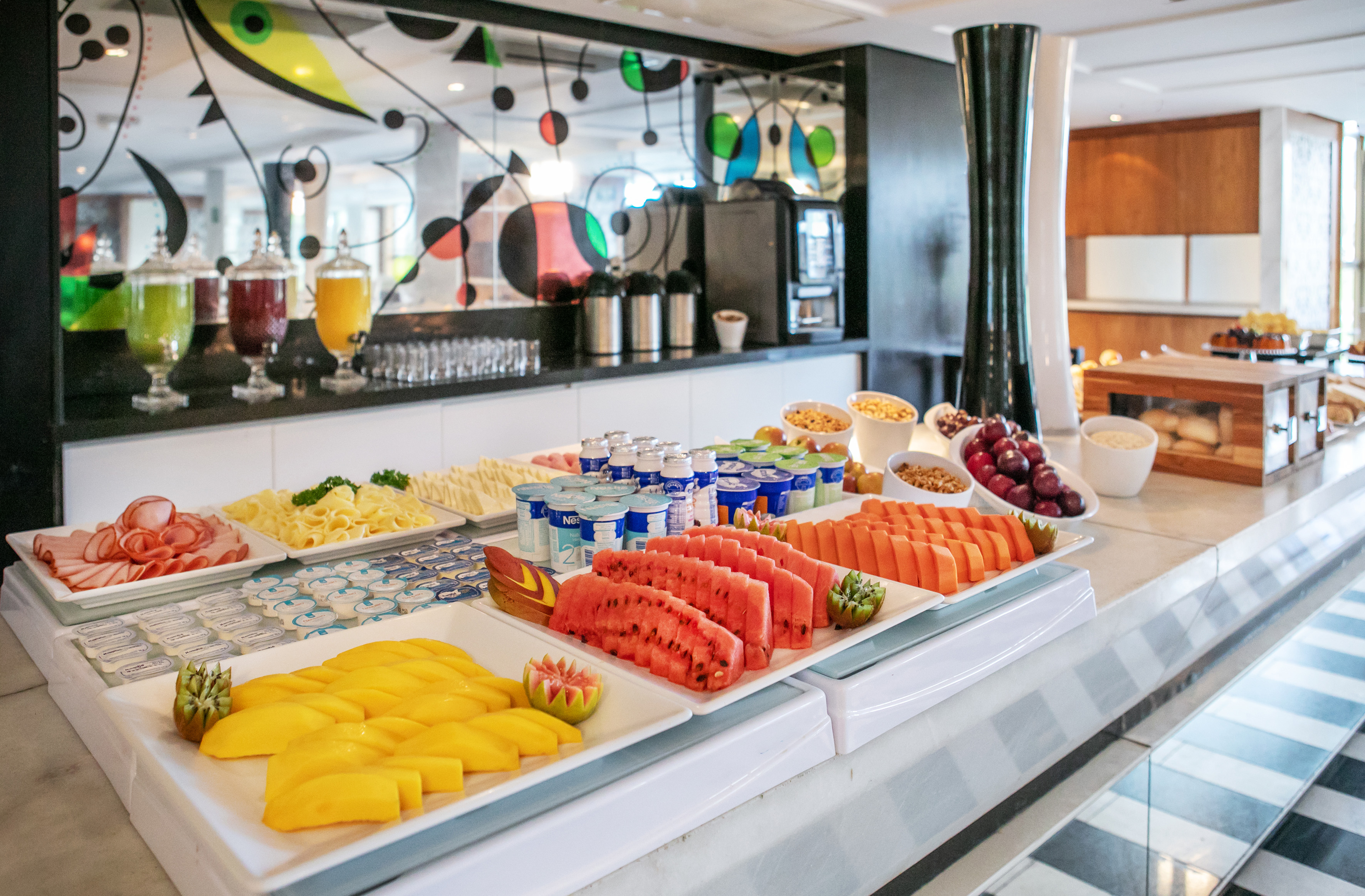 Vibrant hotel breakfast buffet with fresh fruit, cold cuts, yogurt, and juices.