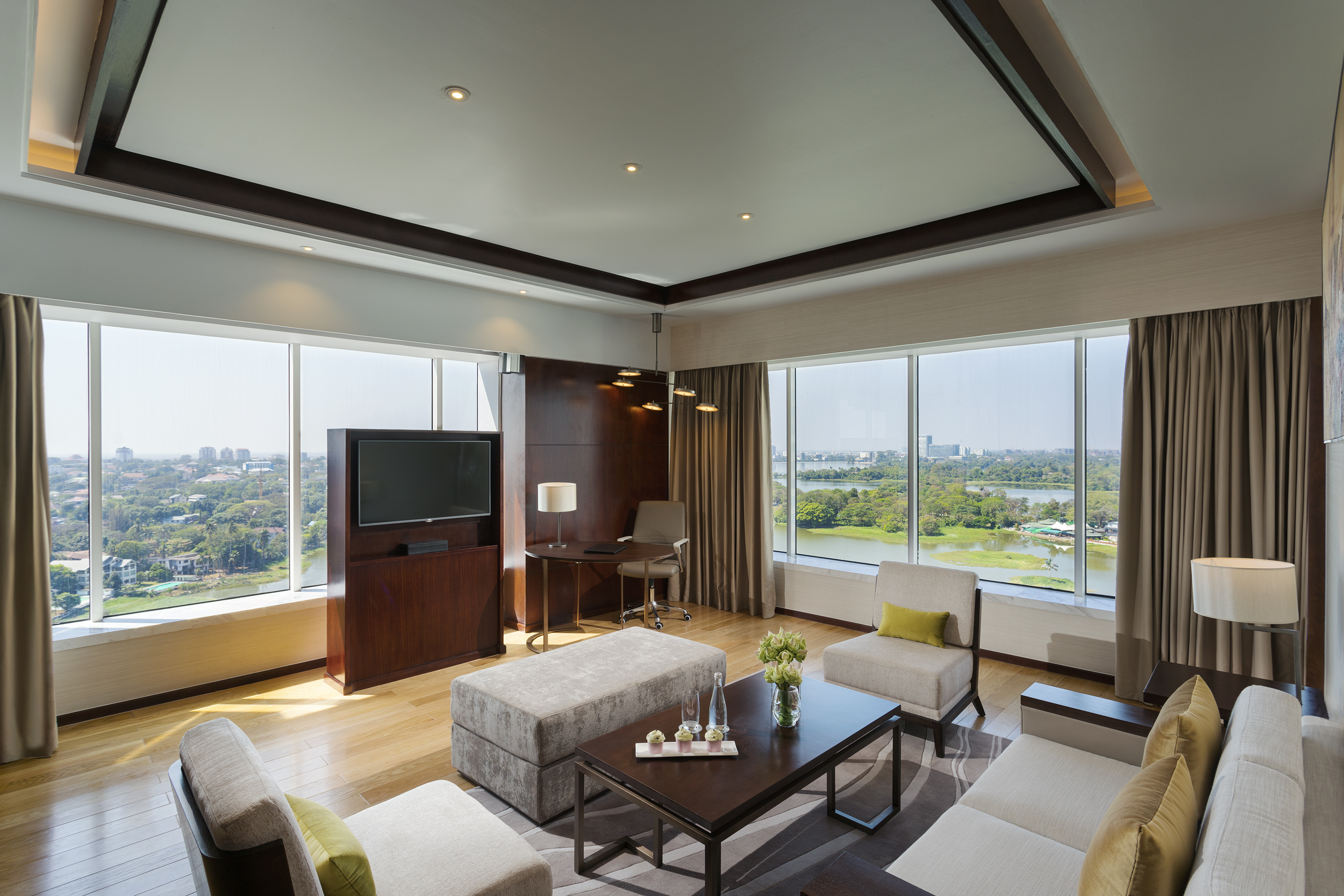 Modern hotel suite: living room with panoramic city & lake views, workspace, TV.