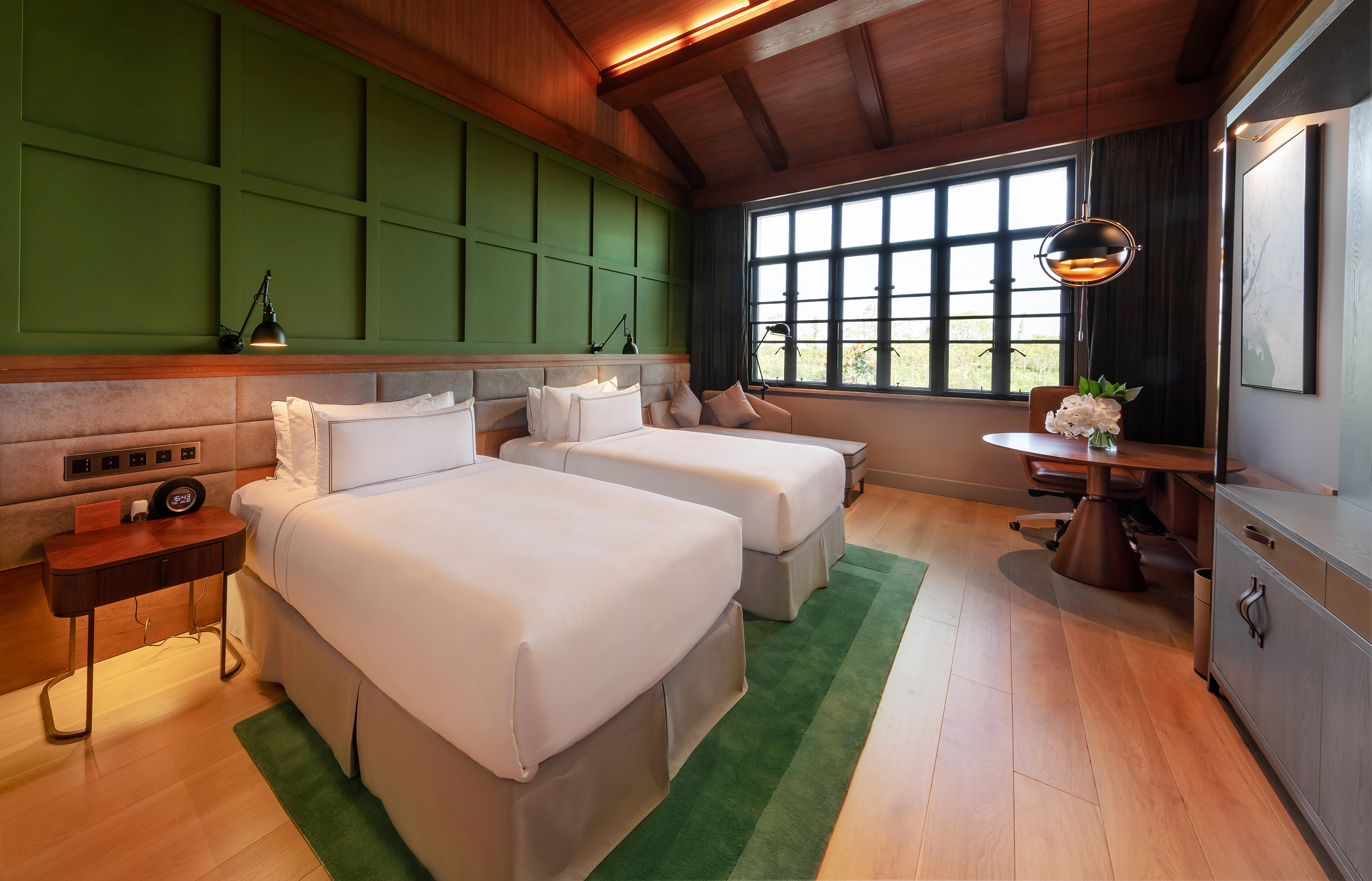 Luxury hotel room with twin beds, green paneled wall, wood ceiling, and work desk.