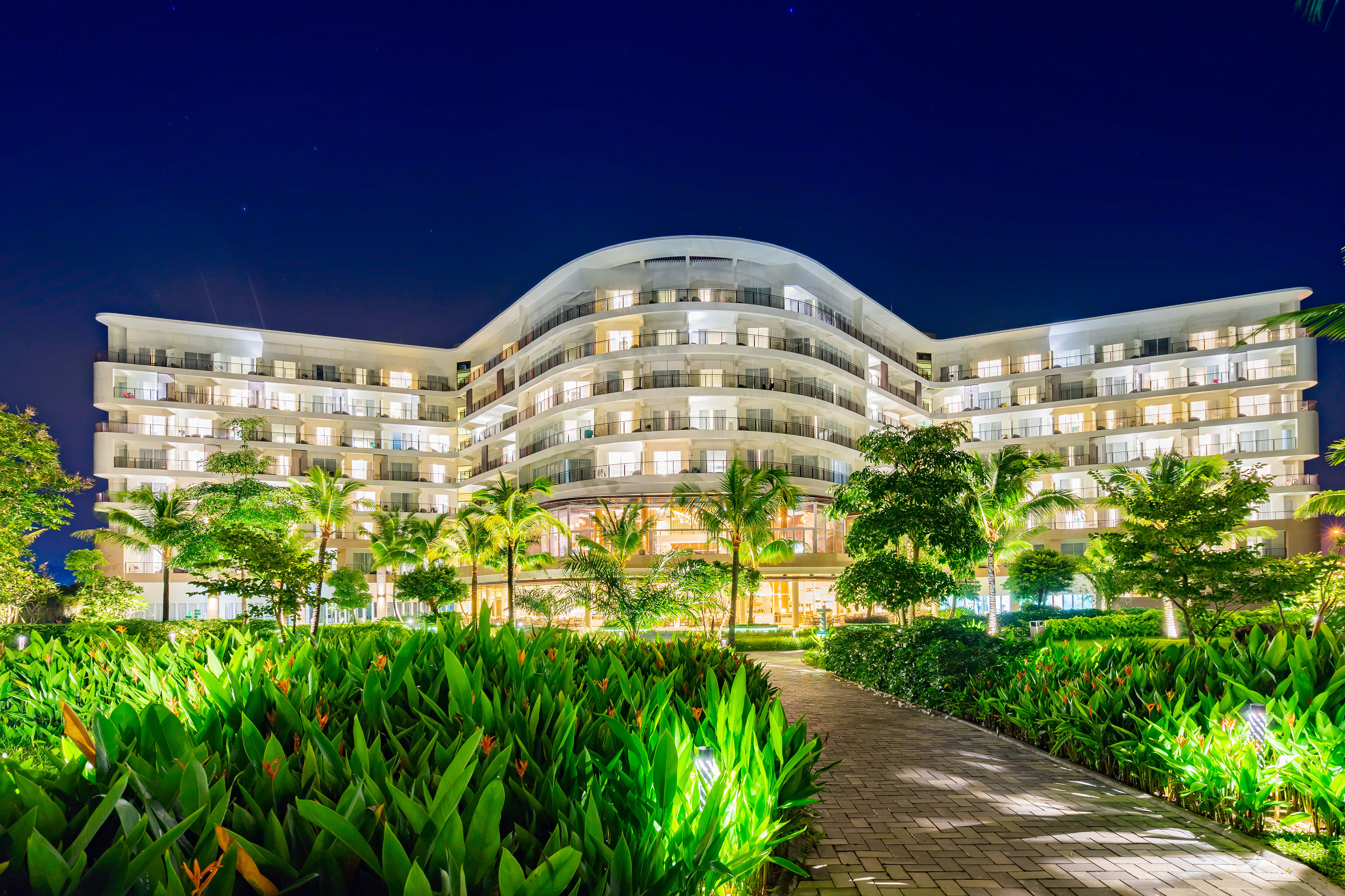 Curved modern resort hotel, lit at night with tropical landscaping.