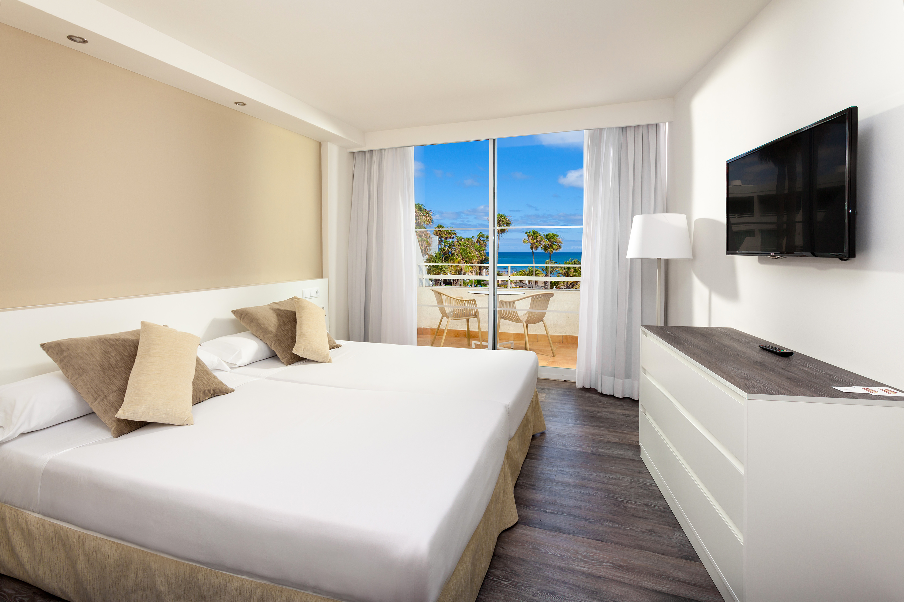 Modern hotel room with ocean view balcony, double bed, and wall-mounted TV.