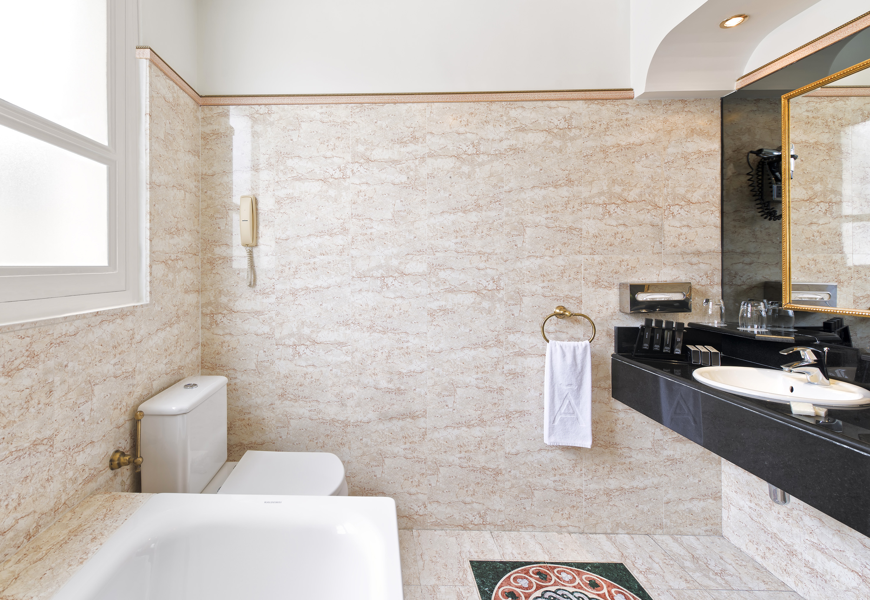 Marble bathroom with white bathtub, toilet, and black vanity sink.