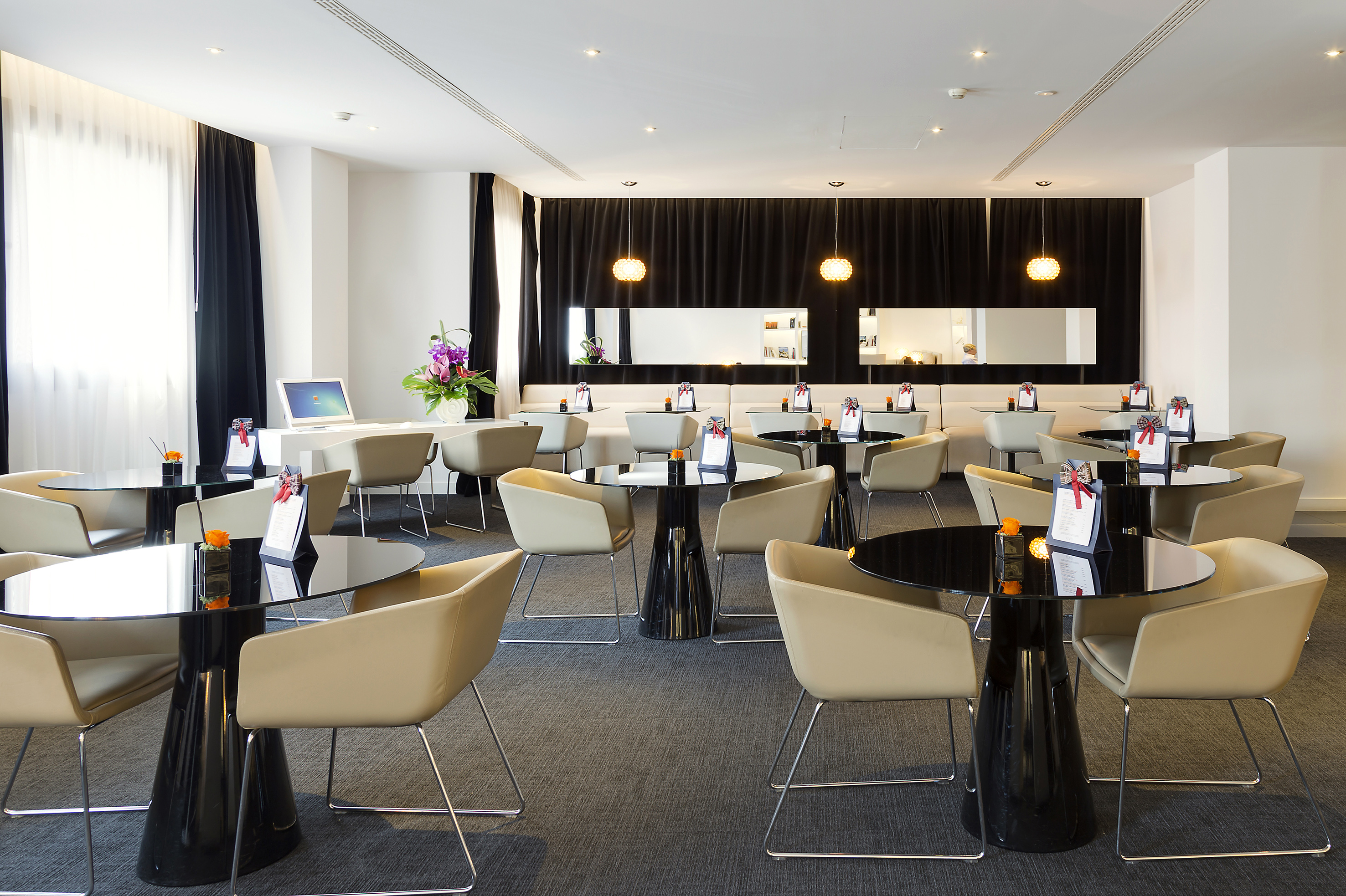 Modern lounge area with black tables, beige chairs, and dark curtains.