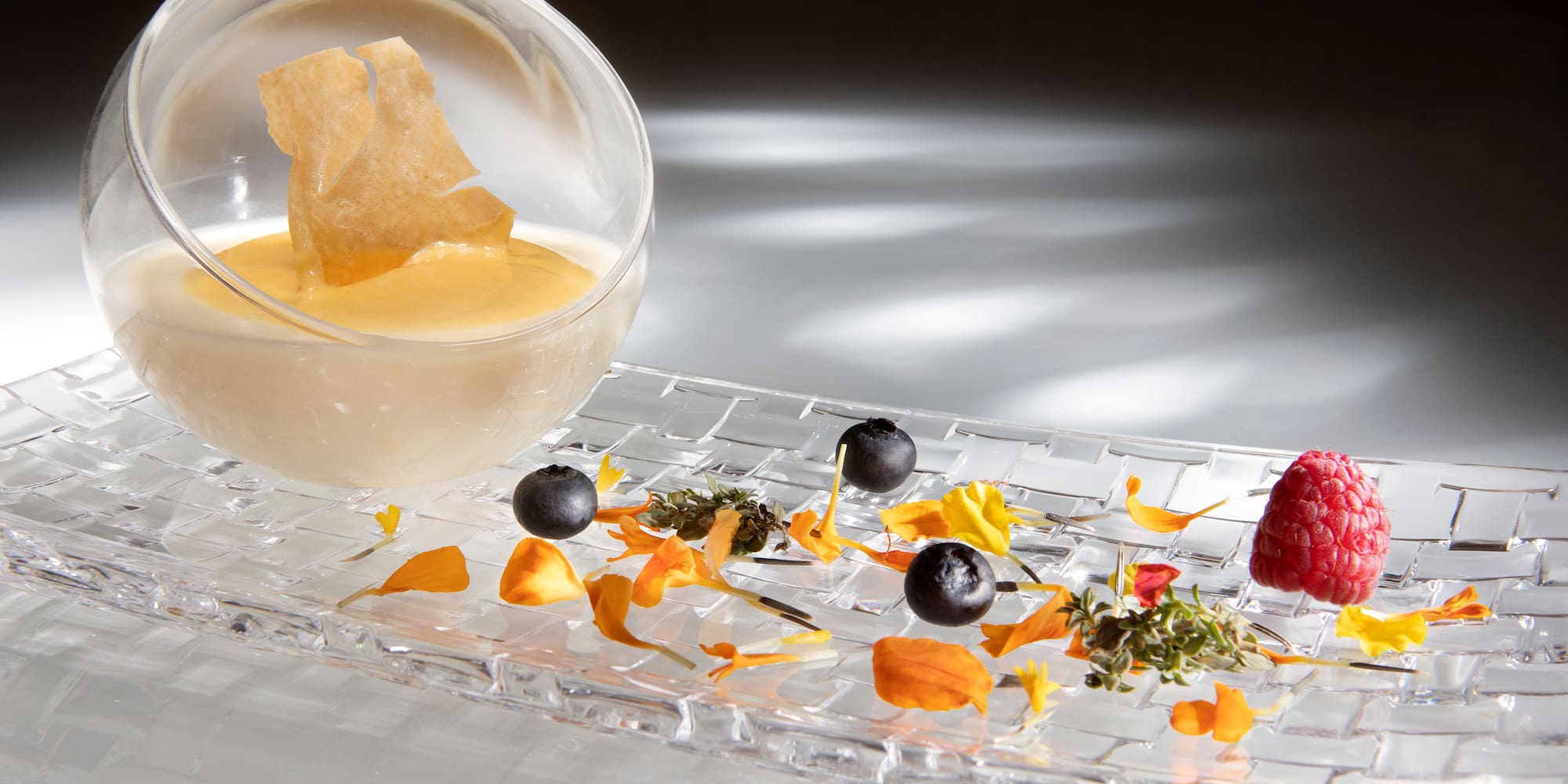 a glass bowl with a bowl of liquid and fruit on a glass plate