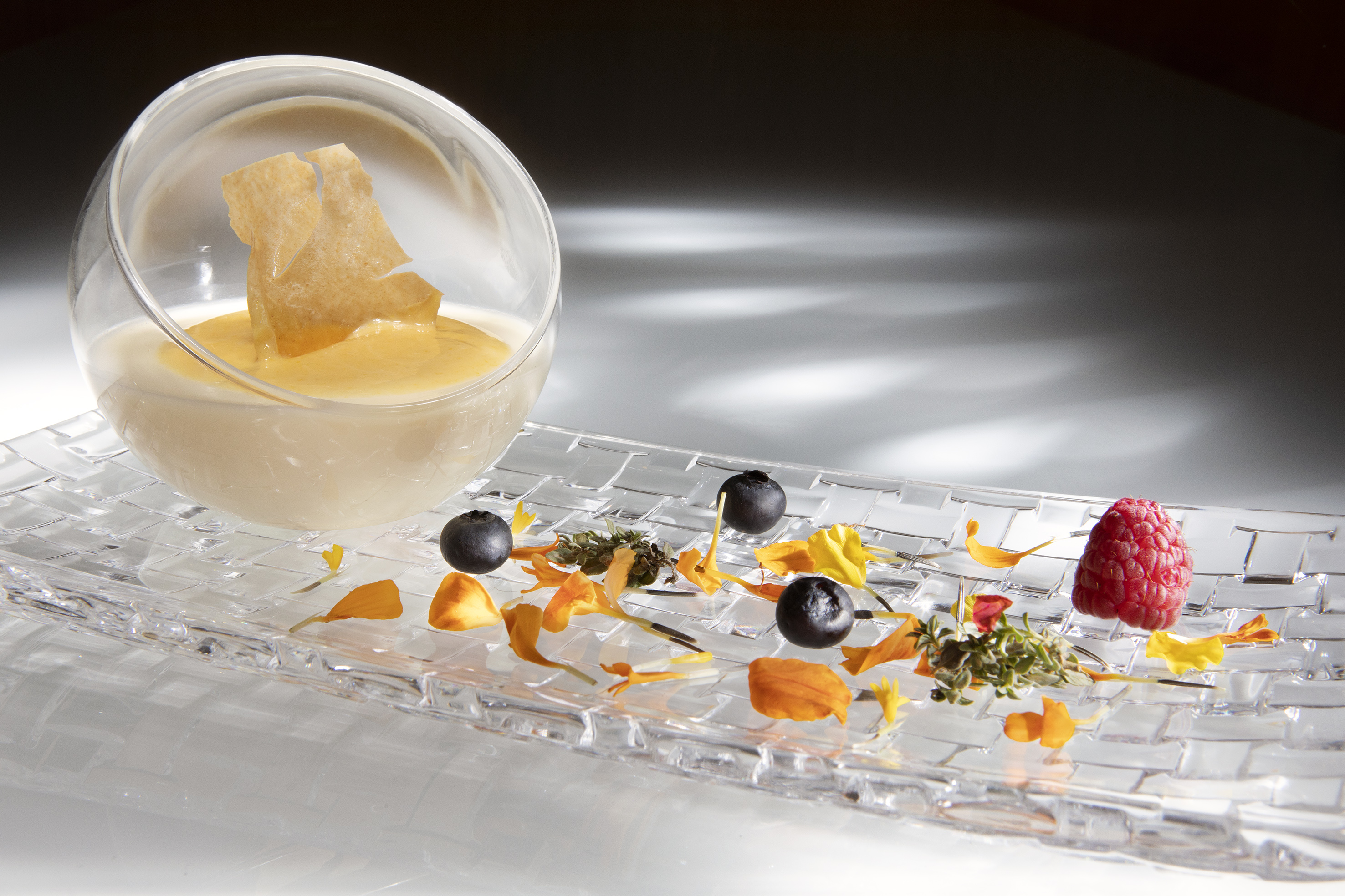 Creamy dessert, yellow topping, wafer, blueberries, raspberry, flower petals.