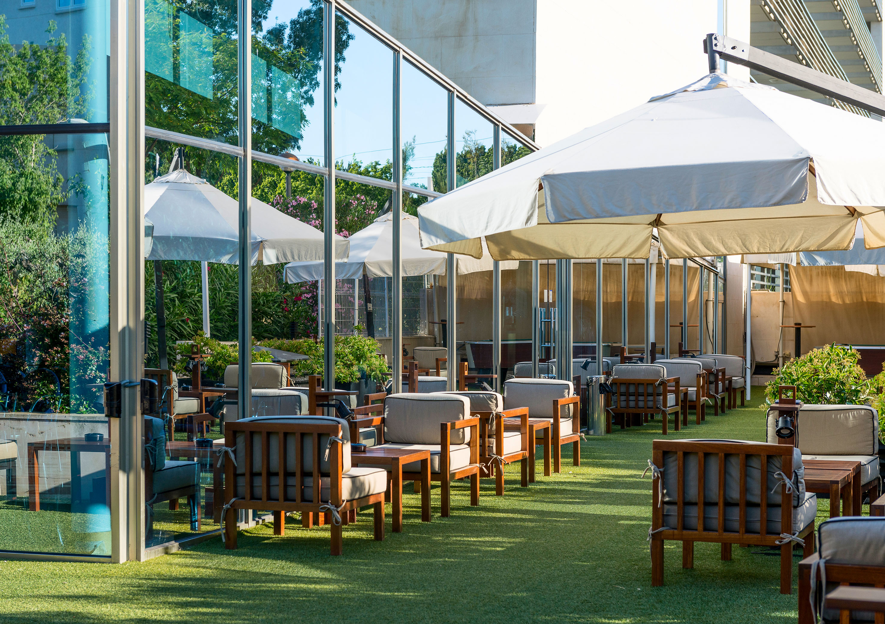 Outdoor lounge patio with wooden furniture, white umbrellas, artificial grass.