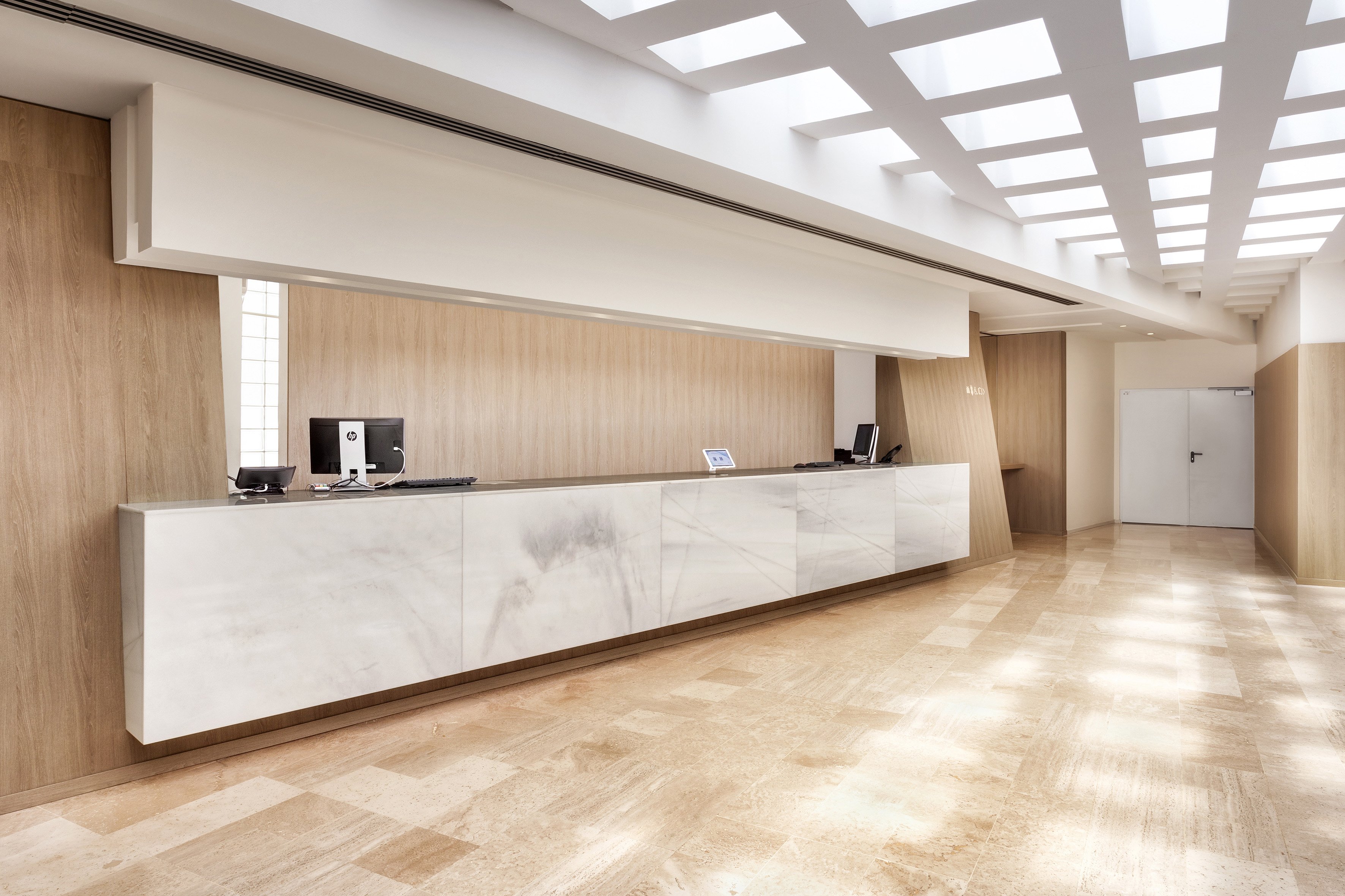 Modern hotel reception desk with white marble, wood walls, and bright ceiling.
