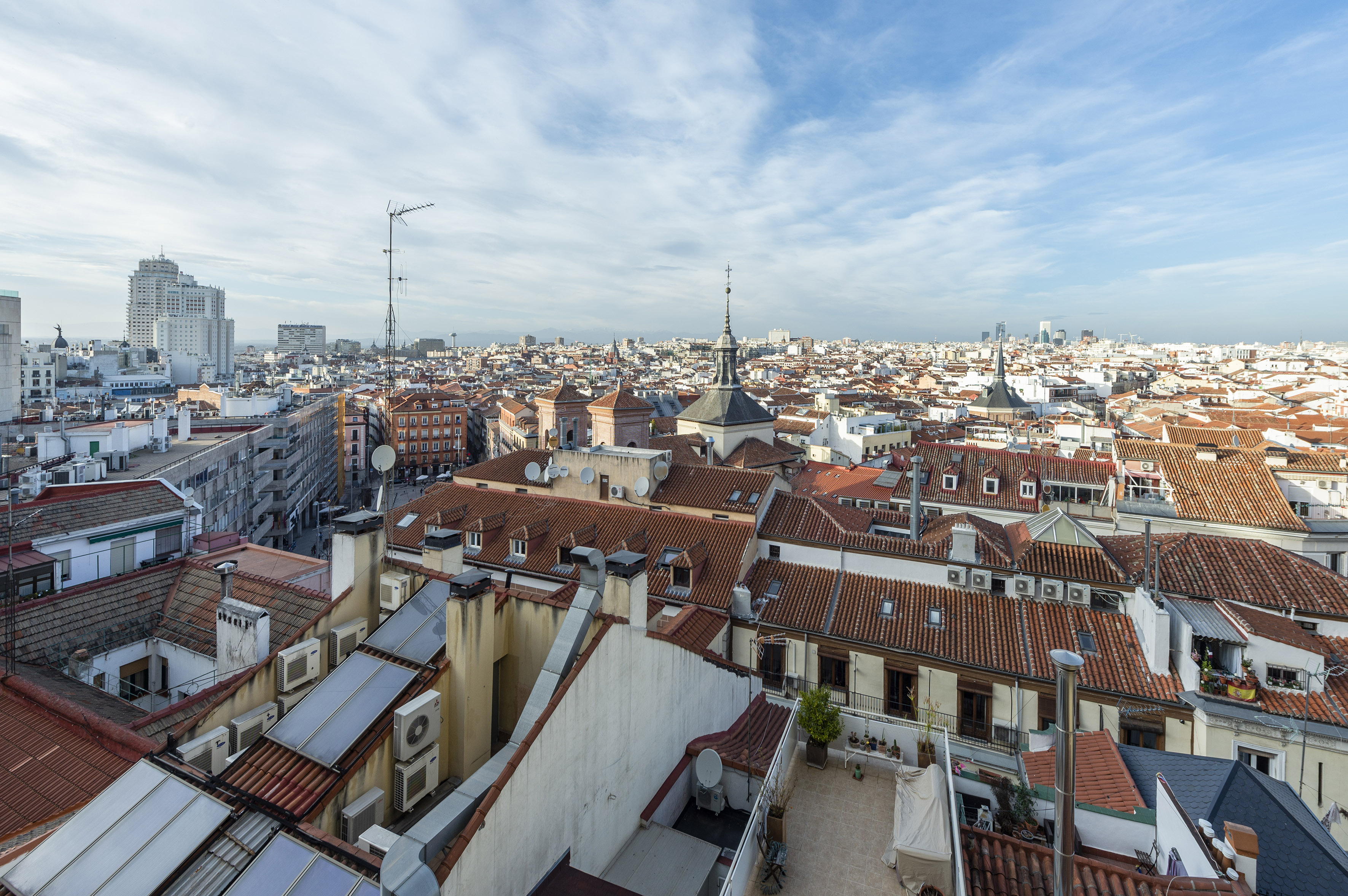 Panoramic Madrid cityscape with red tile rooftops, church spires, and blue sky.
