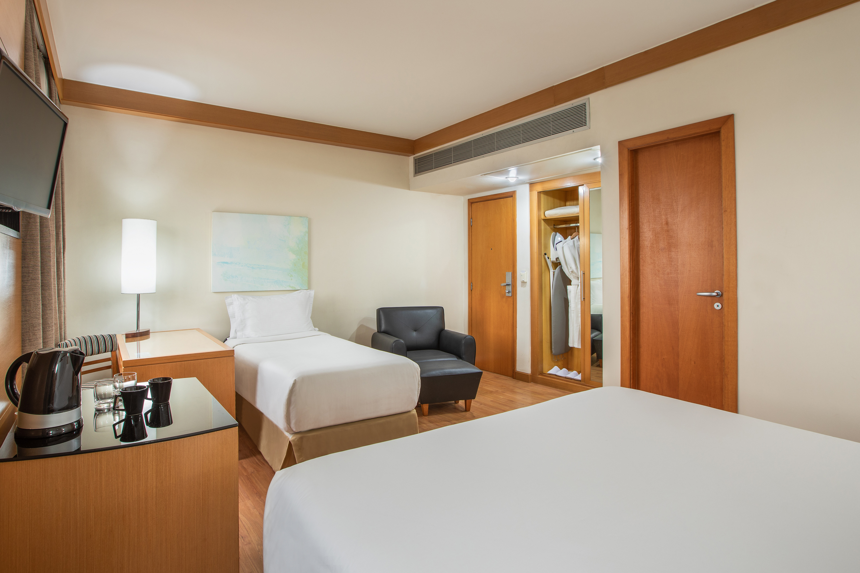 Hotel room with two beds, armchair, nightstand, kettle, and wardrobe.