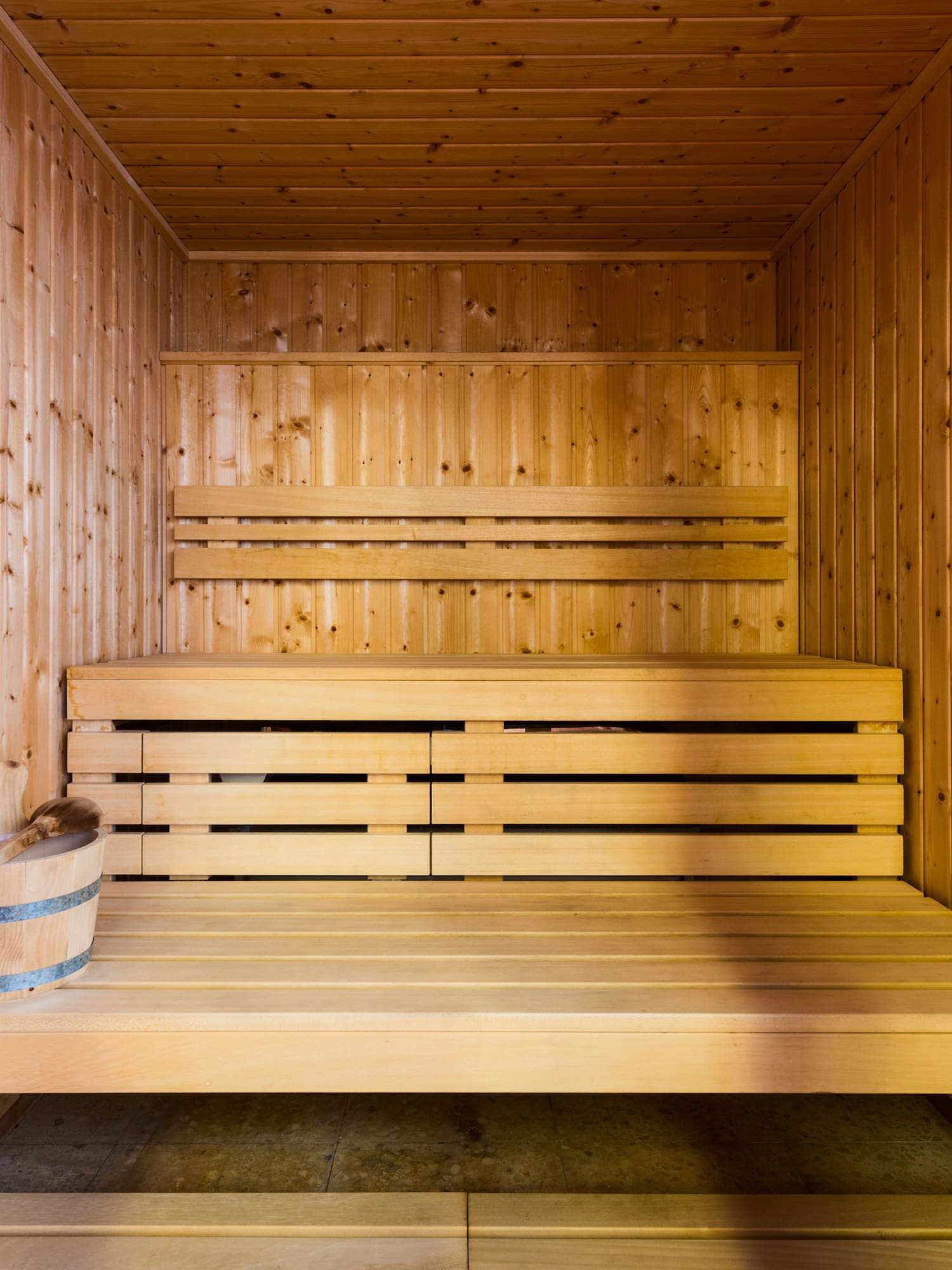 Sauna de madera clara con bancos y accesorios para relajación.