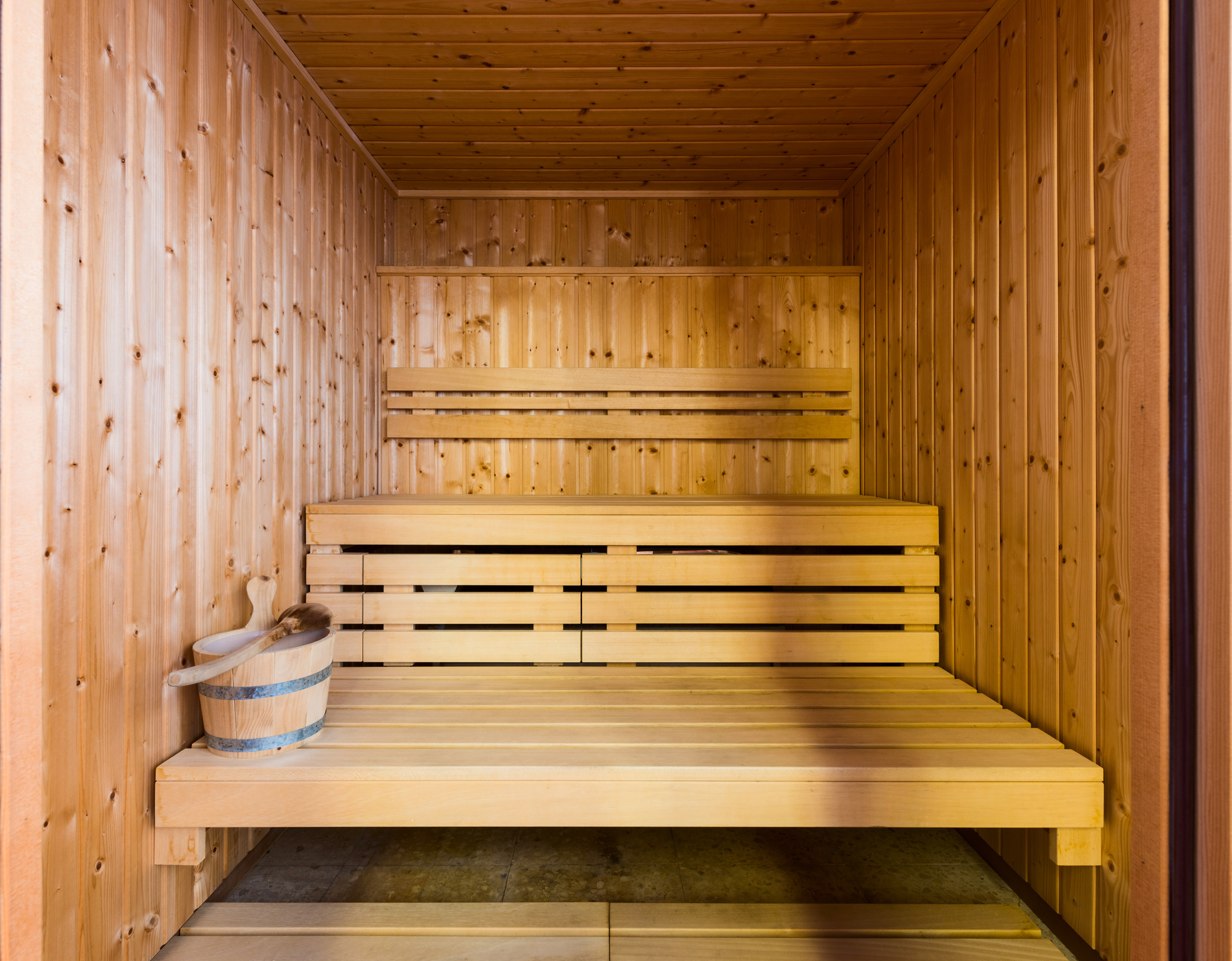 Sauna de madera clara con bancos y accesorios para relajación.