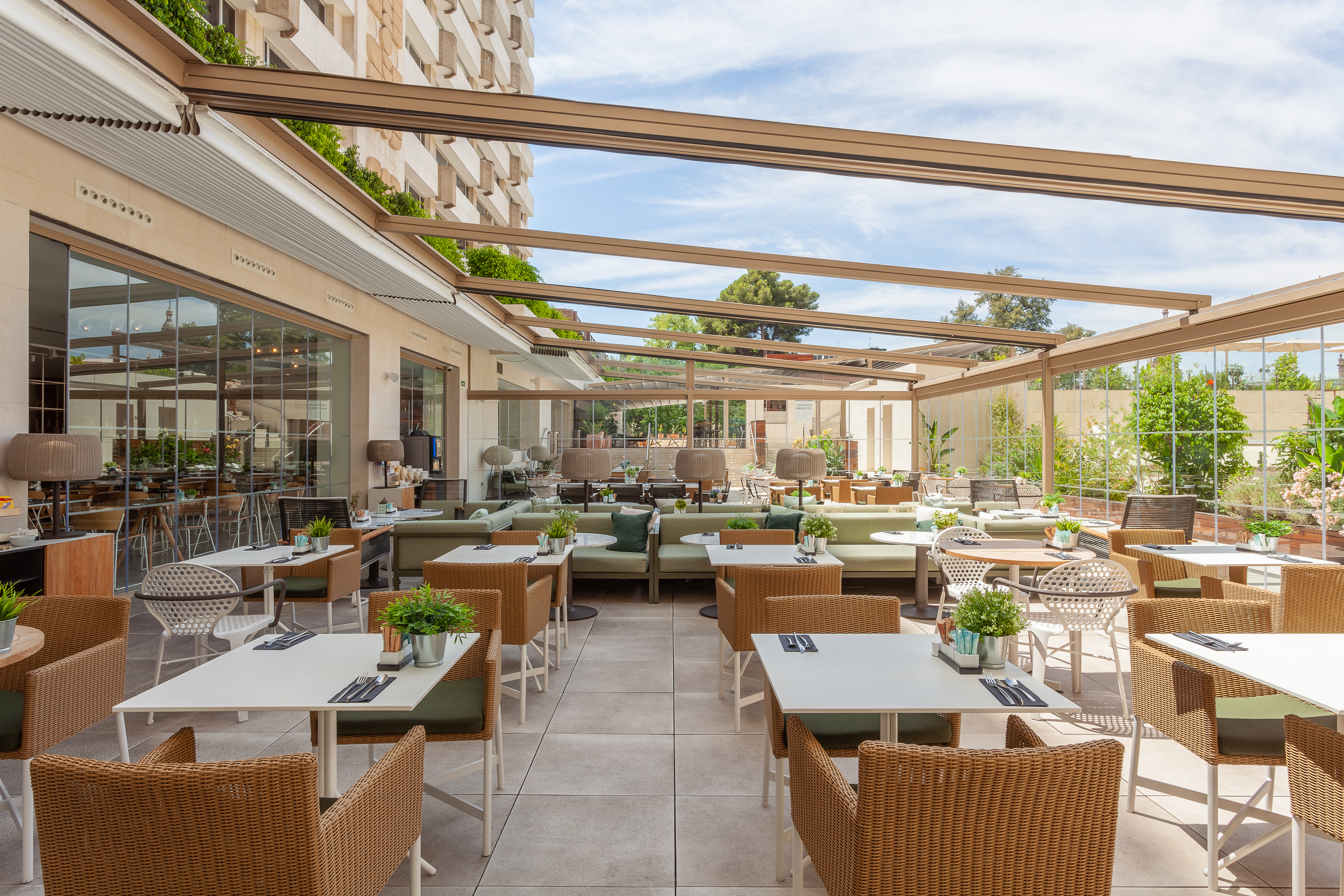 Modern hotel outdoor dining terrace with wicker chairs and a glass roof.
