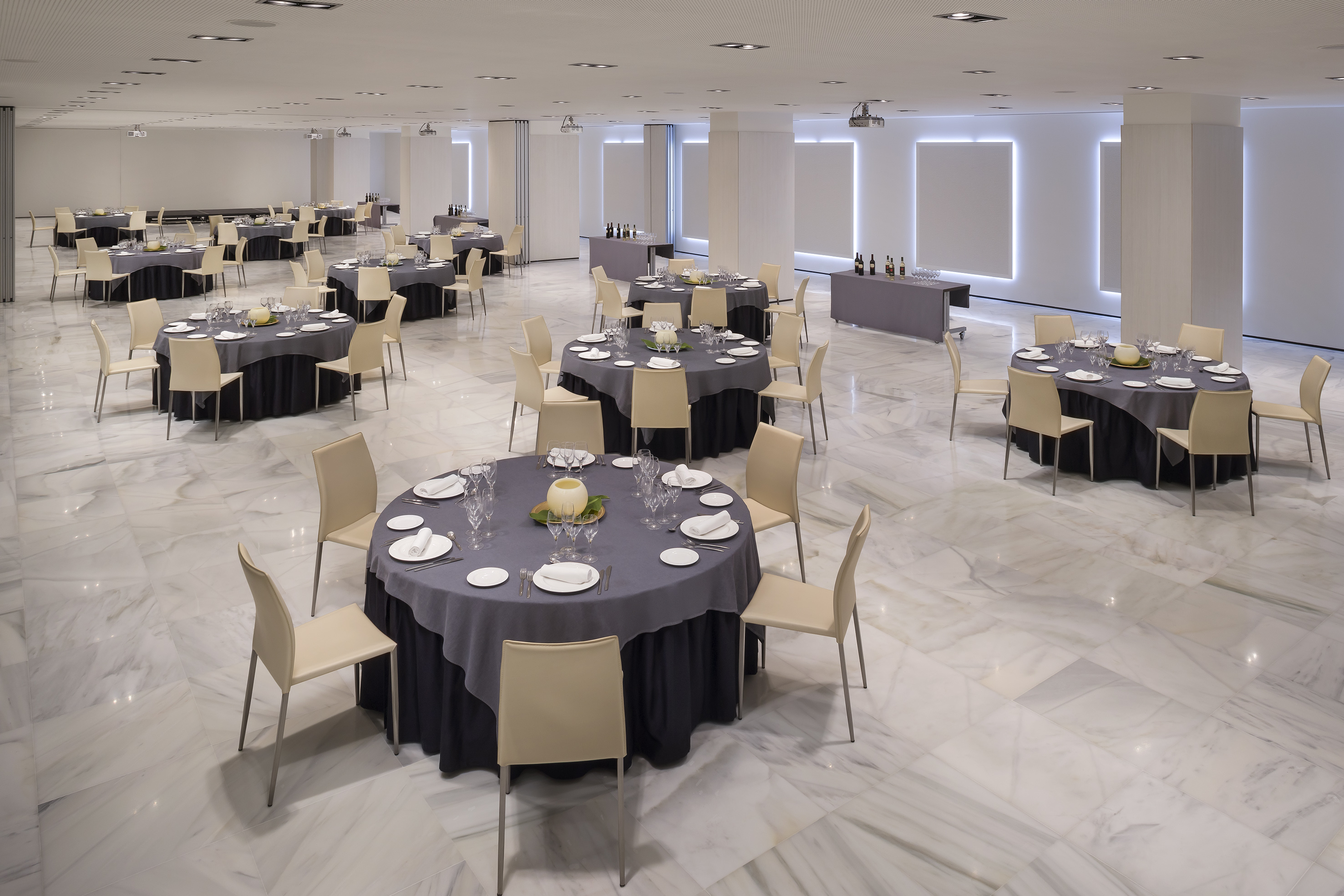 Bright event hall with round dining tables, chairs, and polished marble floor.