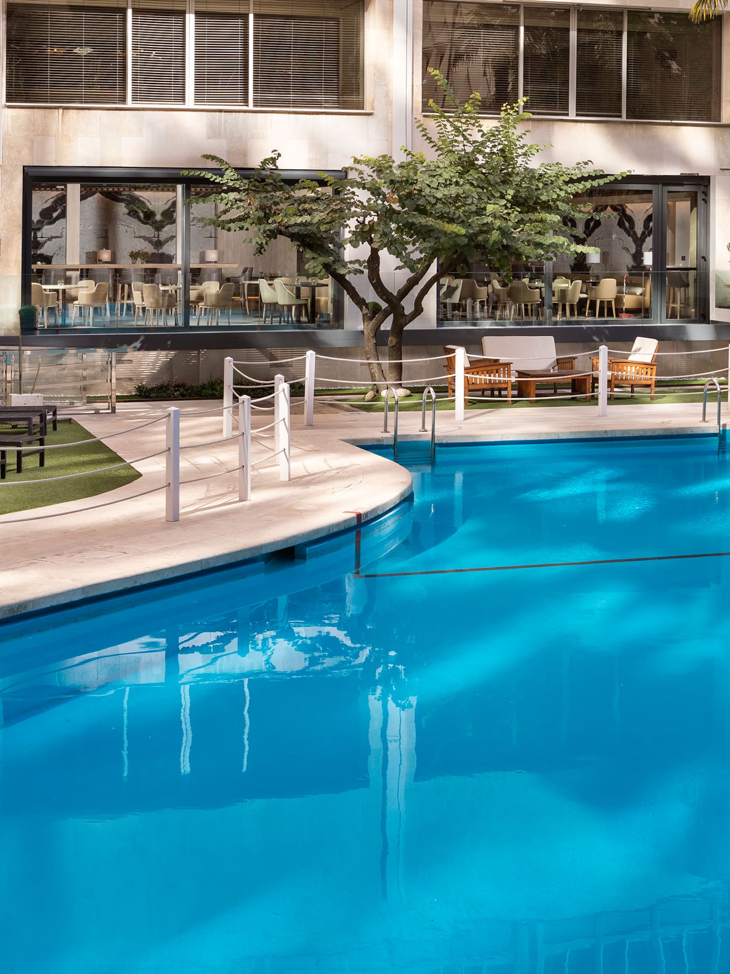 Hotel outdoor swimming pool, sun loungers, palm trees, and modern building.