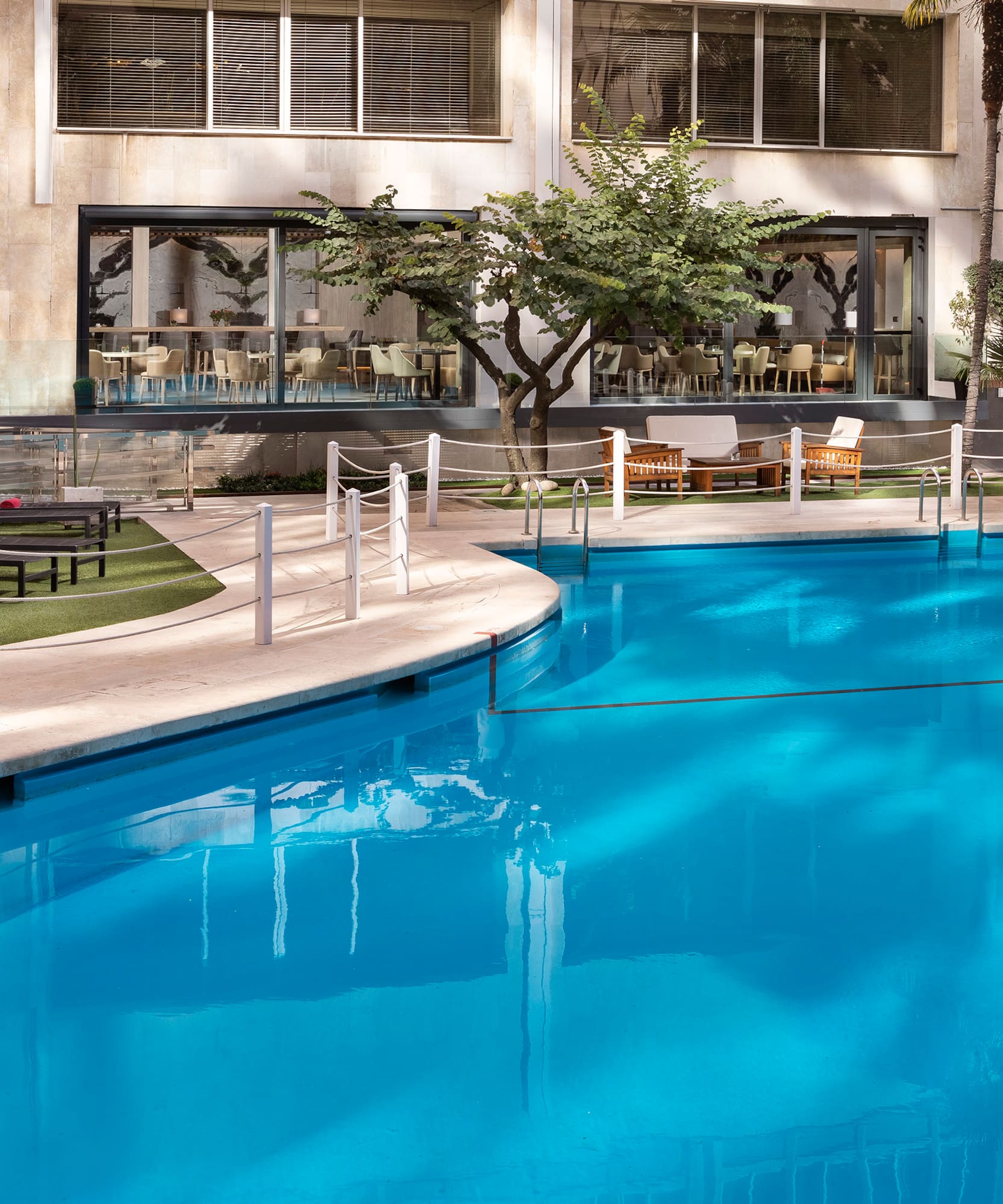 Hotel outdoor swimming pool, sun loungers, palm trees, and modern building.