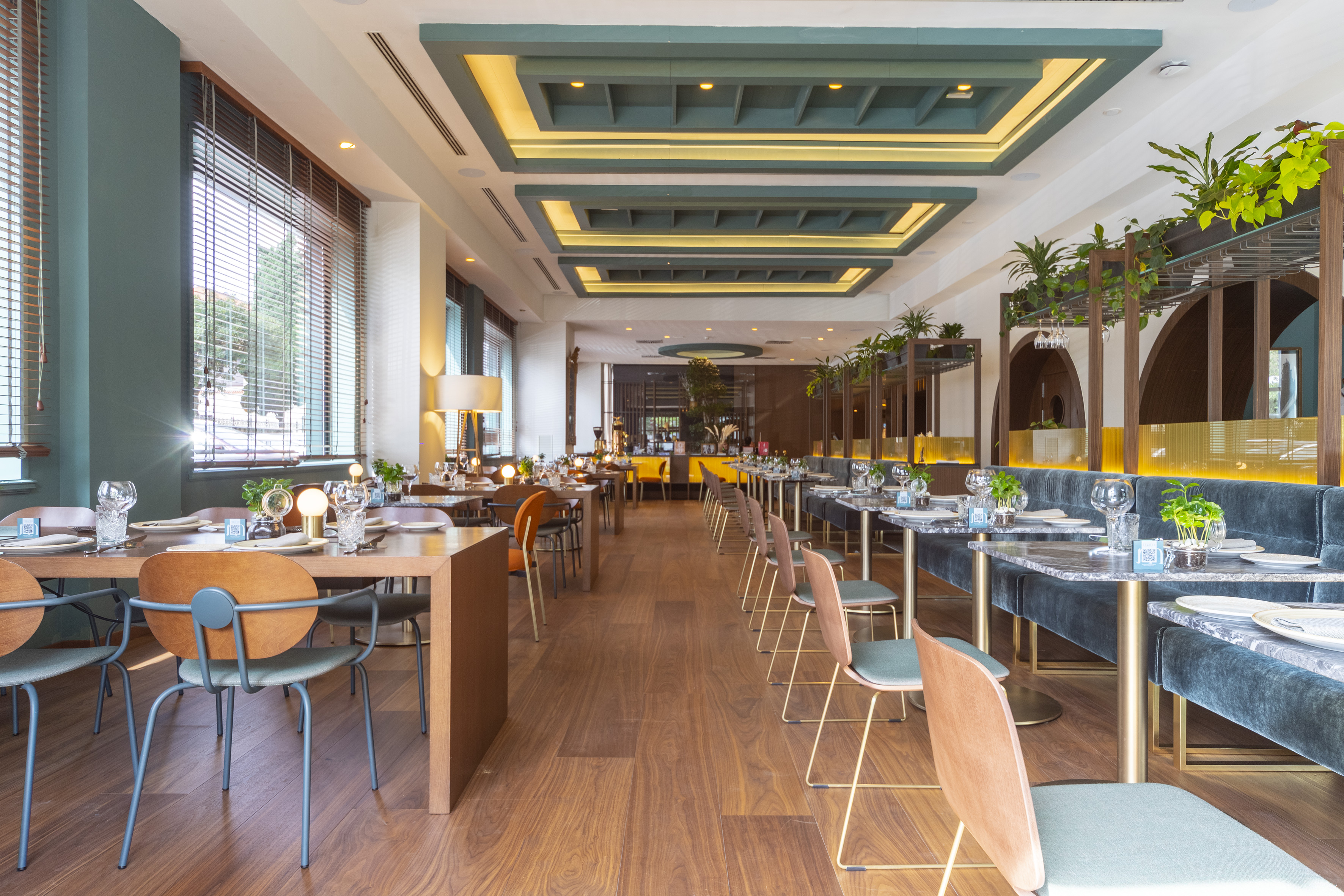 Modern restaurant dining room with set tables, wooden floor, and teal accents.