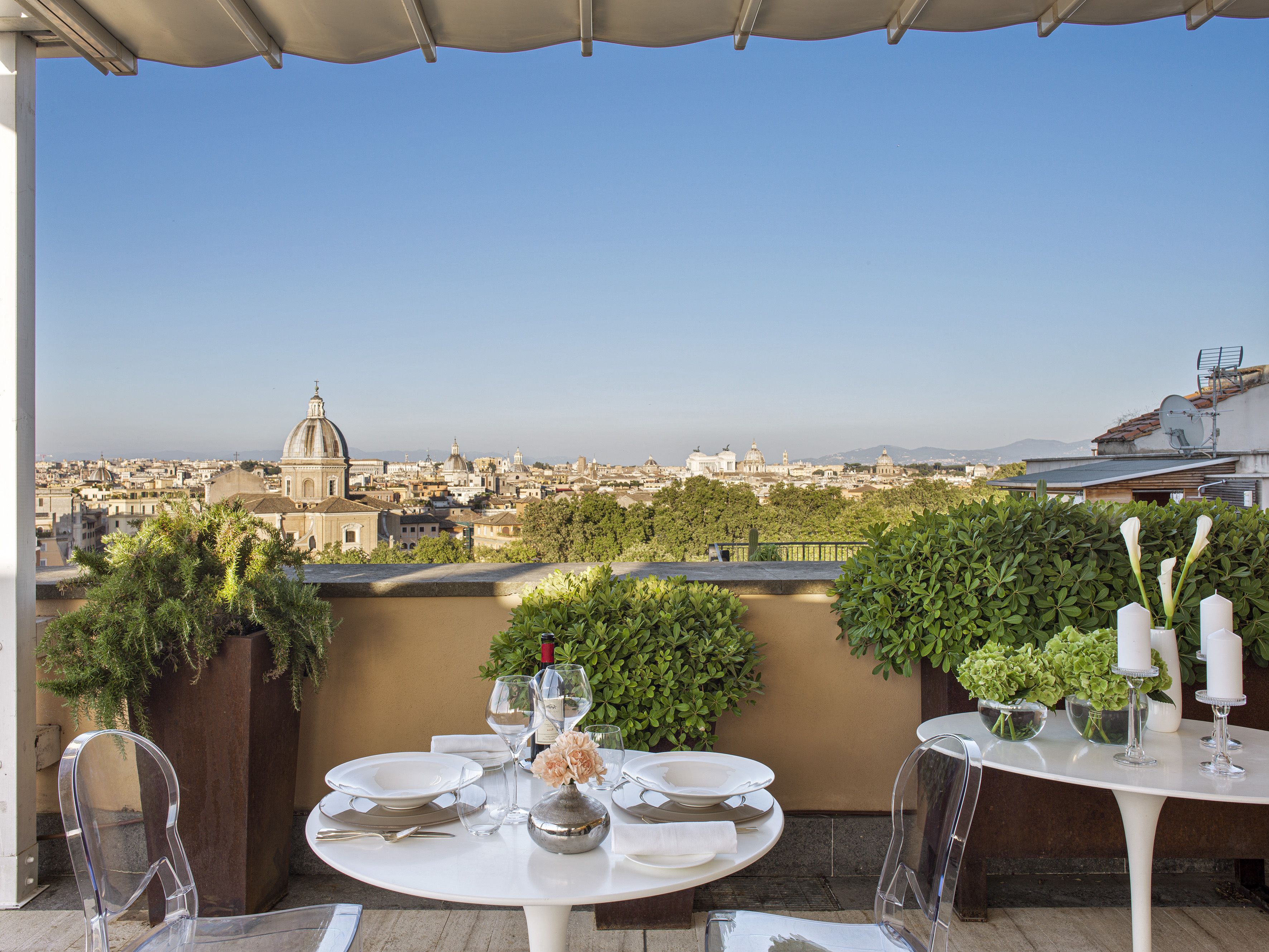 Hotel rooftop terrace with dining table overlooking Rome's cityscape.
