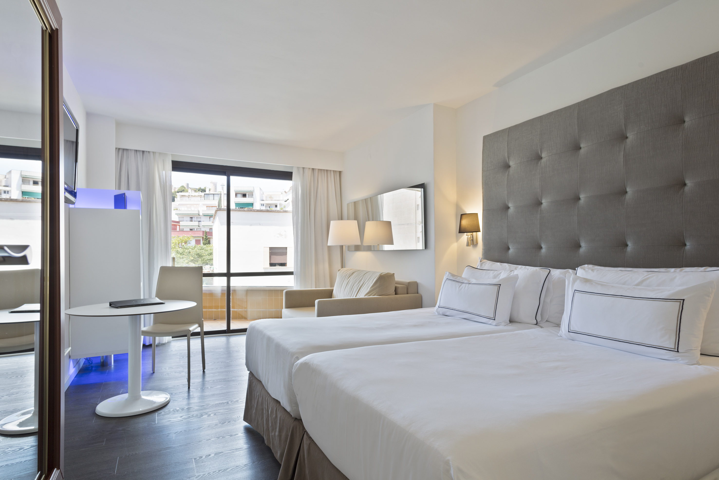 Modern hotel twin room with city view, dark floor, and grey headboard.
