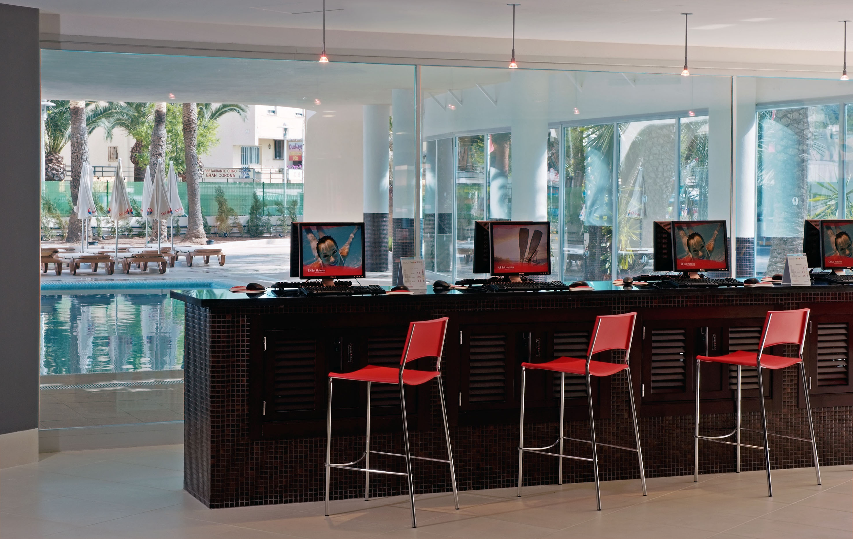Hotel internet cafe with red stools, desktop PCs, and swimming pool view.