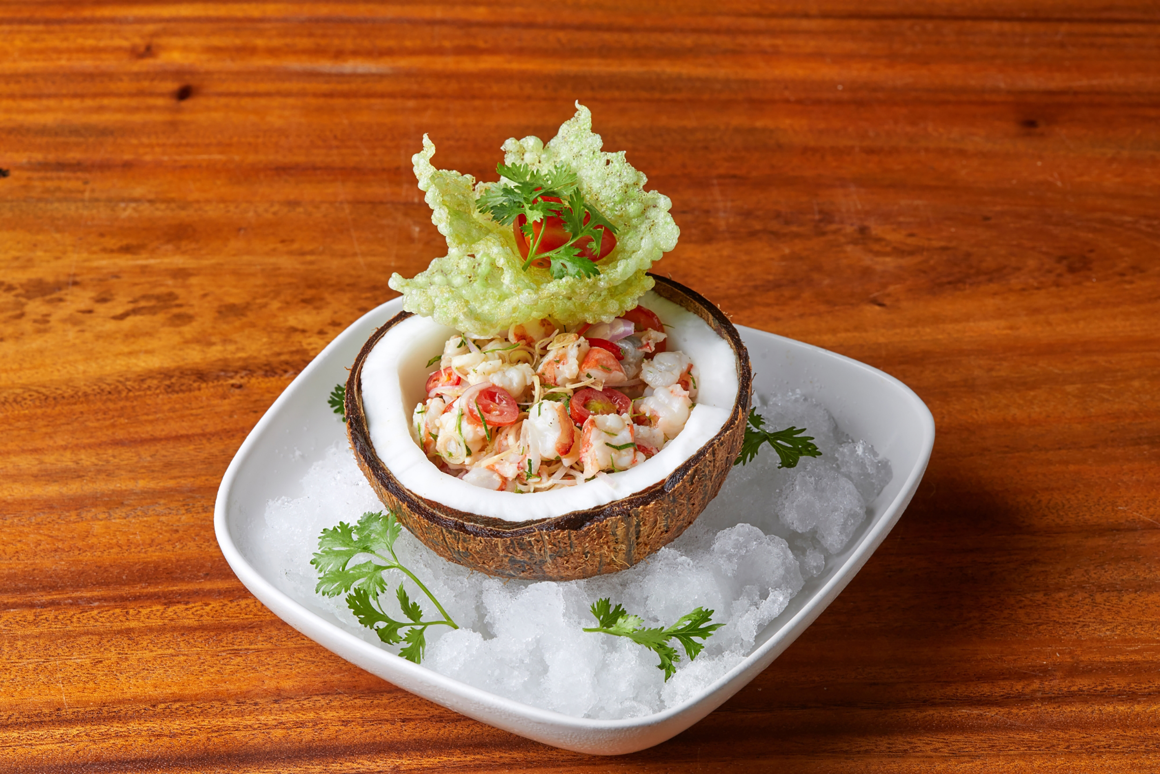 Tropical shrimp salad in a coconut shell, garnished with crisp and tomatoes.