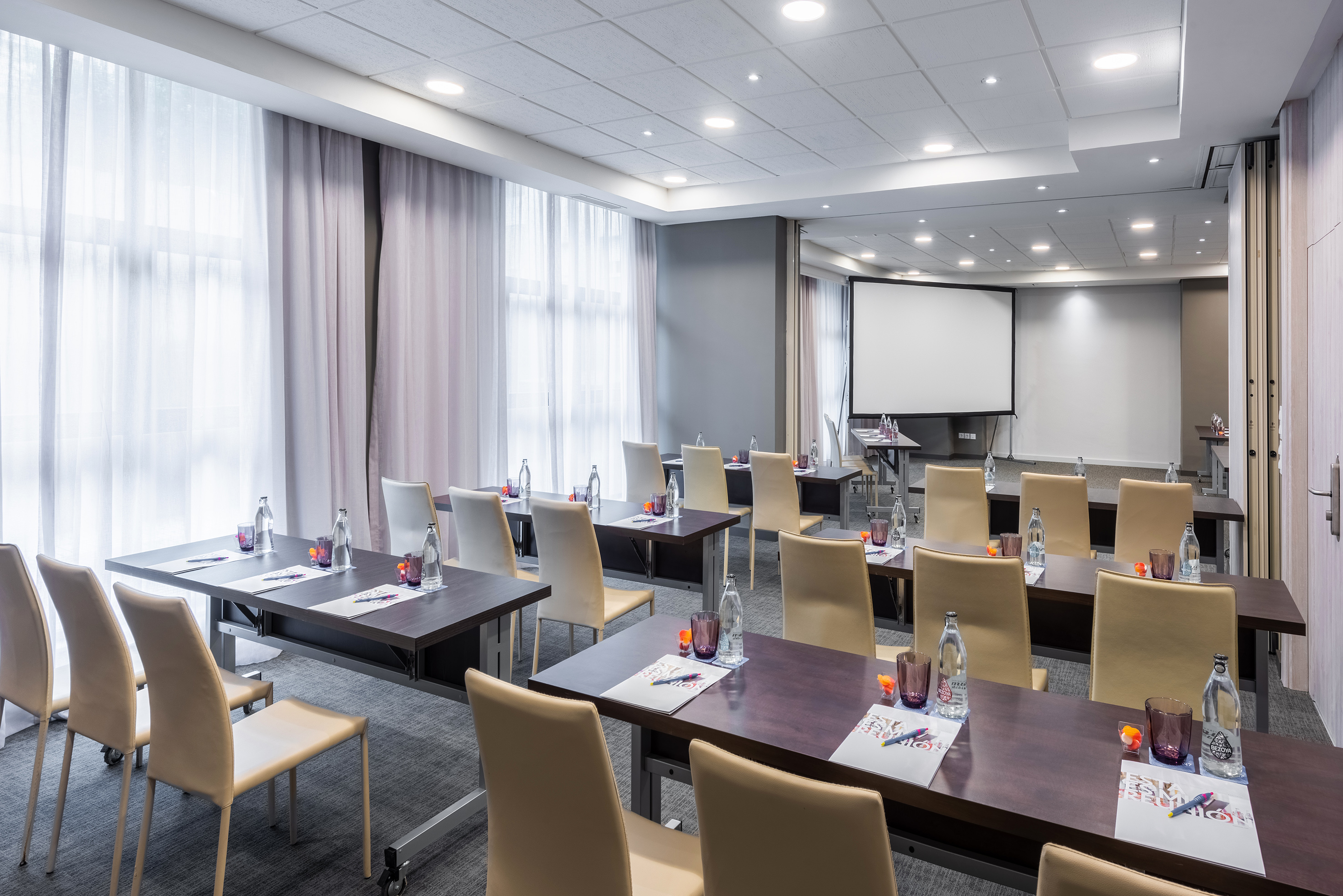 Modern meeting room with tables, chairs, and projection screen for events.